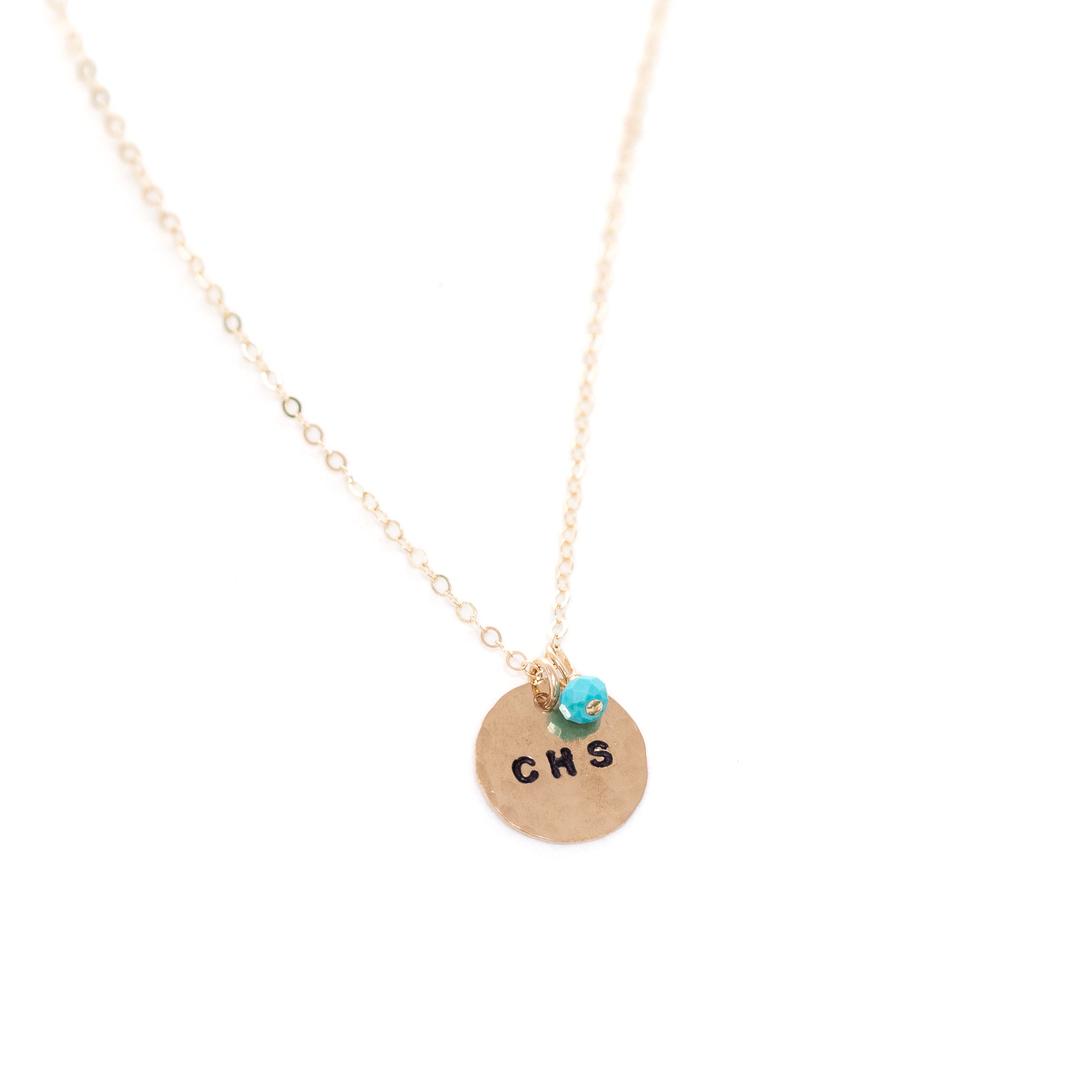 A gold circle stamped necklace with the additional turquoise bead hanging from it. 