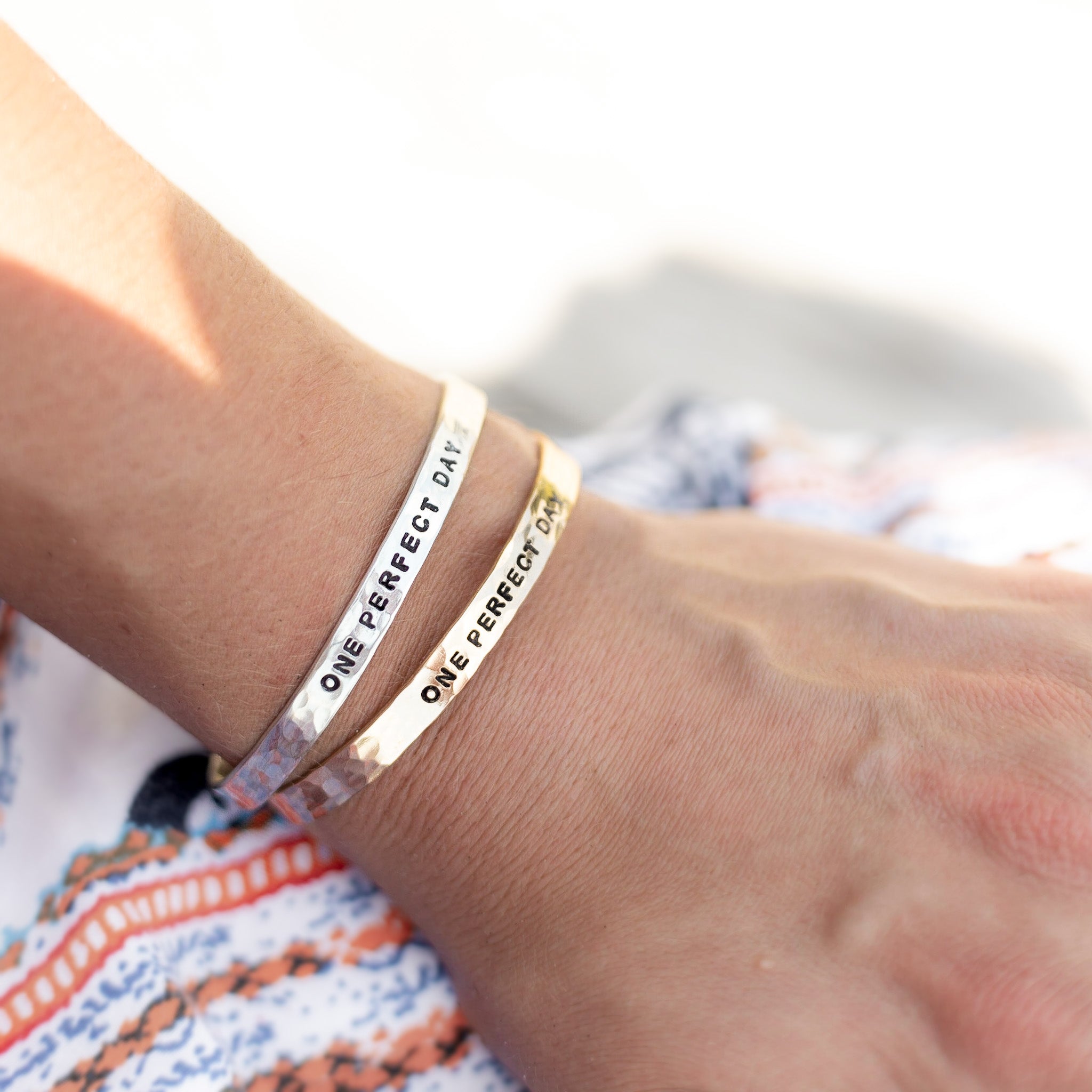 A gold filled and sterling silver cuff with the phrase "one perfect day" on it. Shown on a woman's wrist.