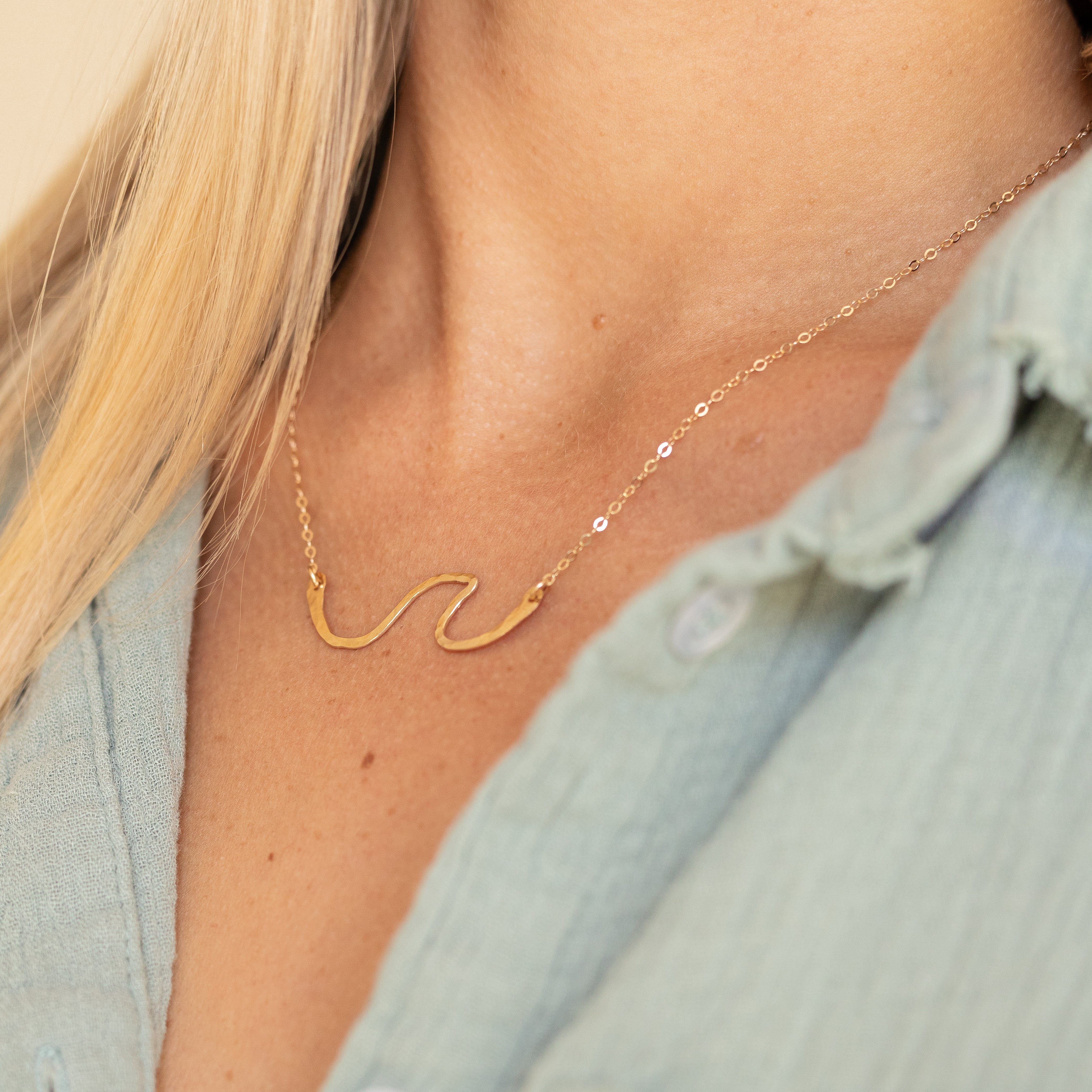 Hand forged gold filled wave with gold wire on a chain shown on a woman's neck. 