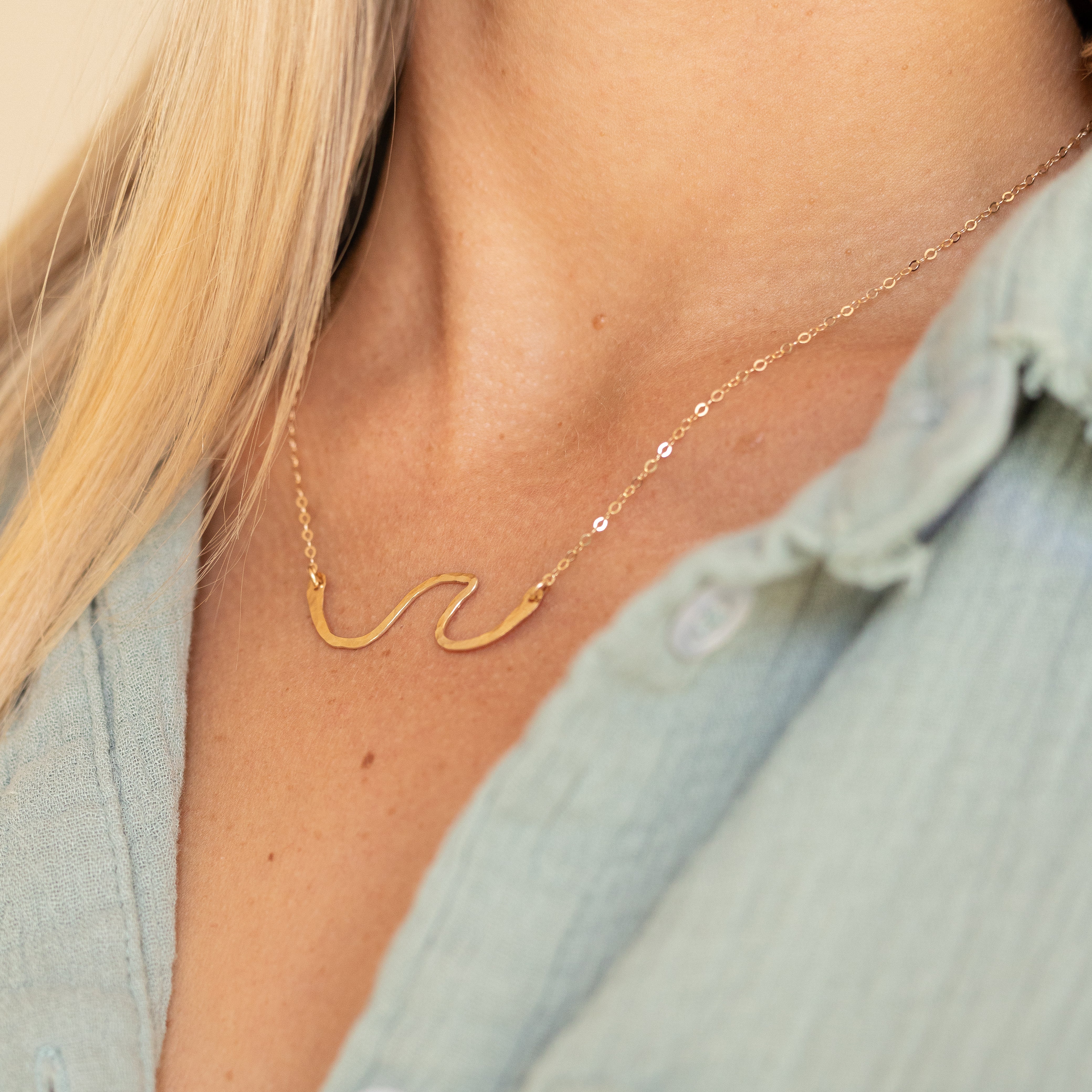 Hand forged gold filled wave with gold wire on a chain shown on a woman's neck.
