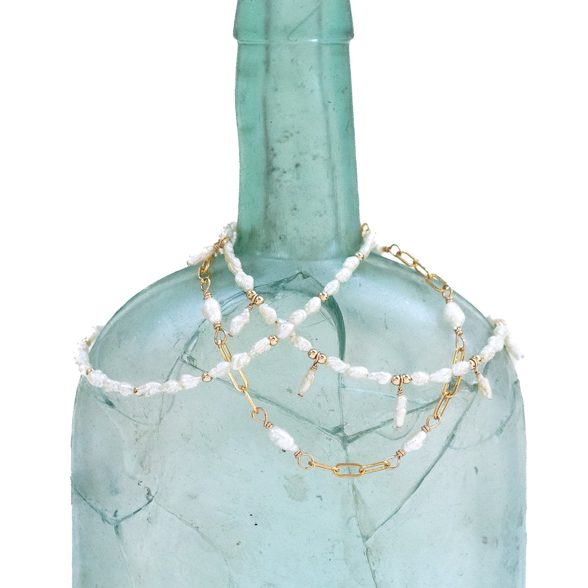 Three different variations of the tiny pearl bracelet displayed on a bottle