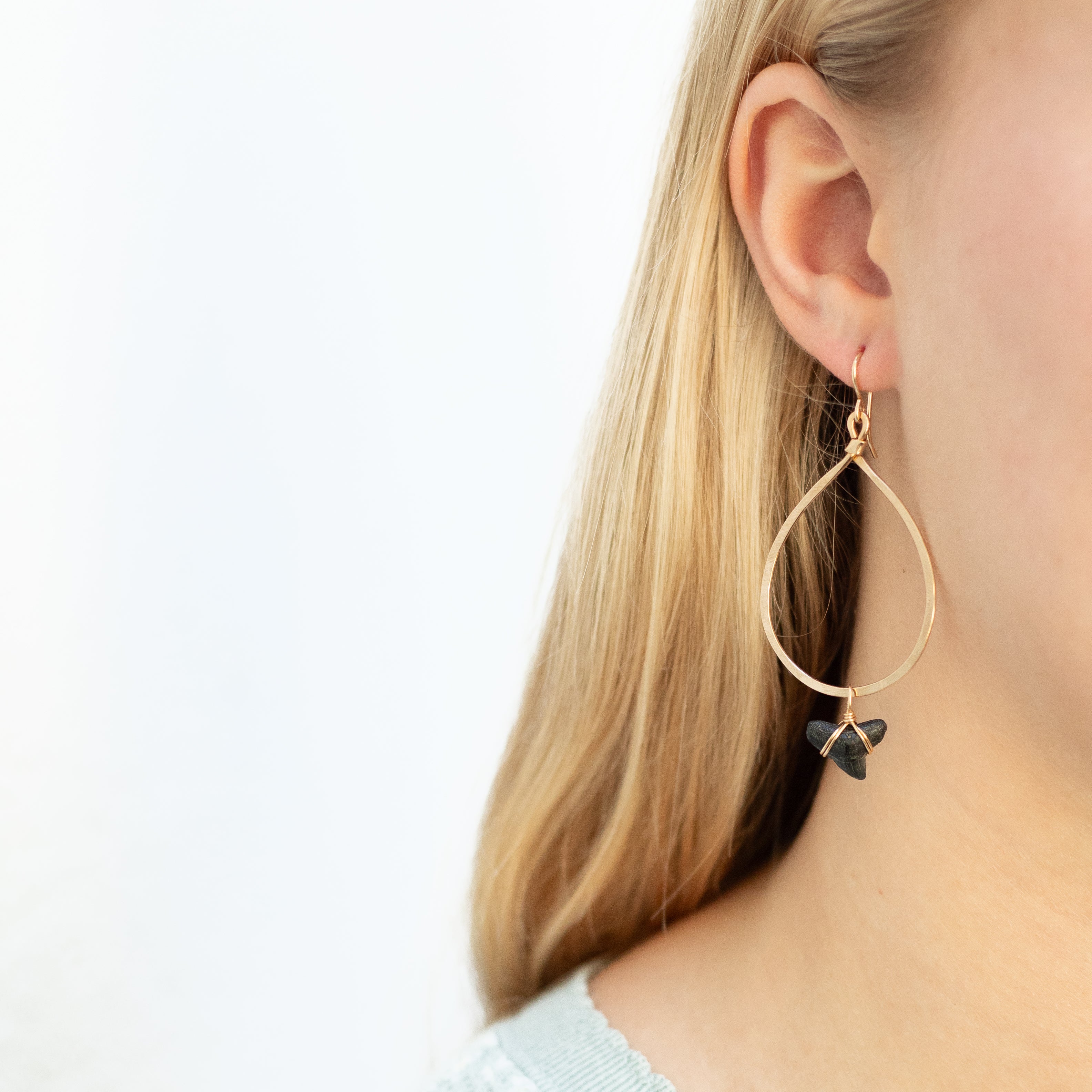 Smaller gold hoop with shark tooth attached to the hoop with gold wire. Seen dangling in woman’s ear.