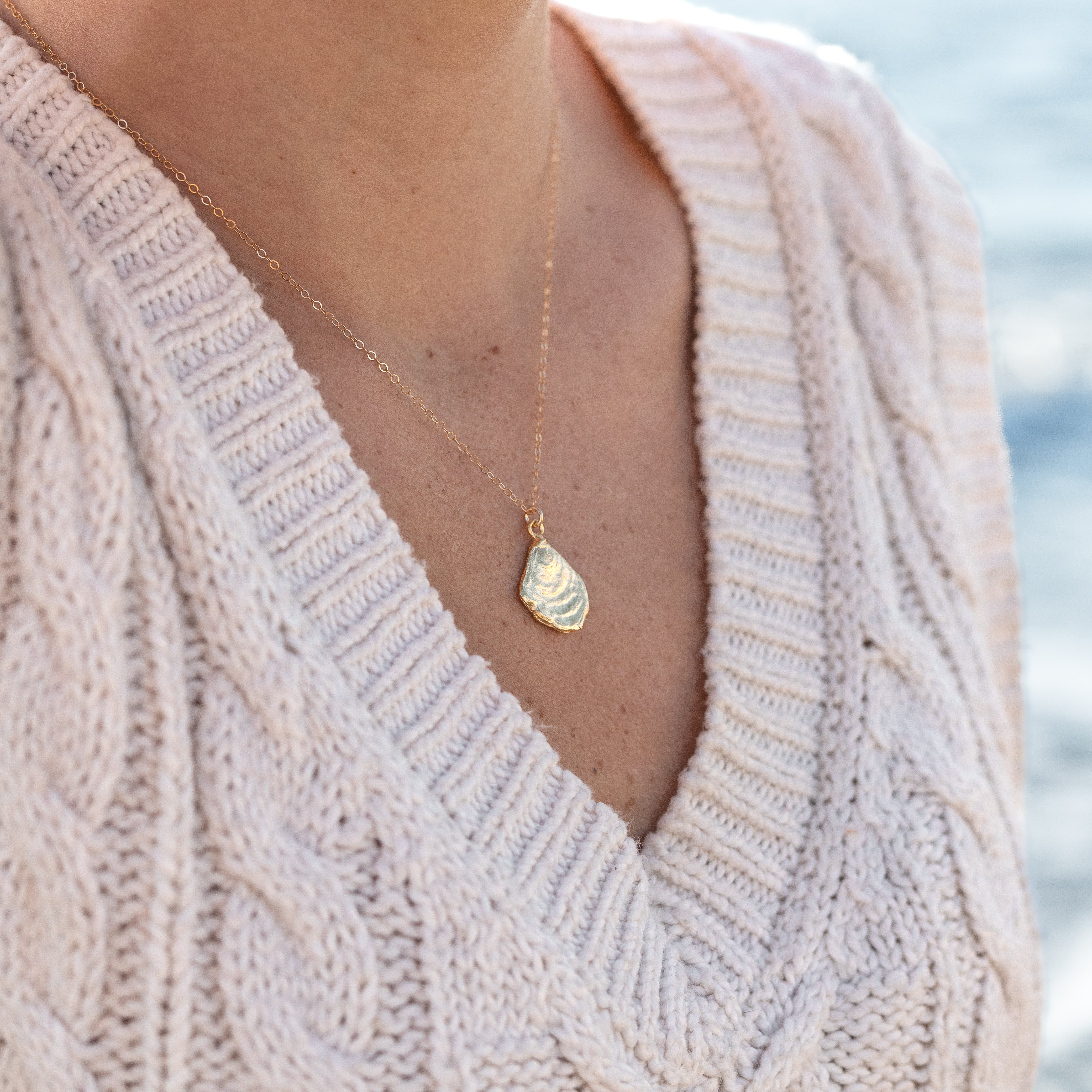 Small gold dipped oyster shell charm attached to a 14 carrot gold chain. Shown on a woman’s neck.
