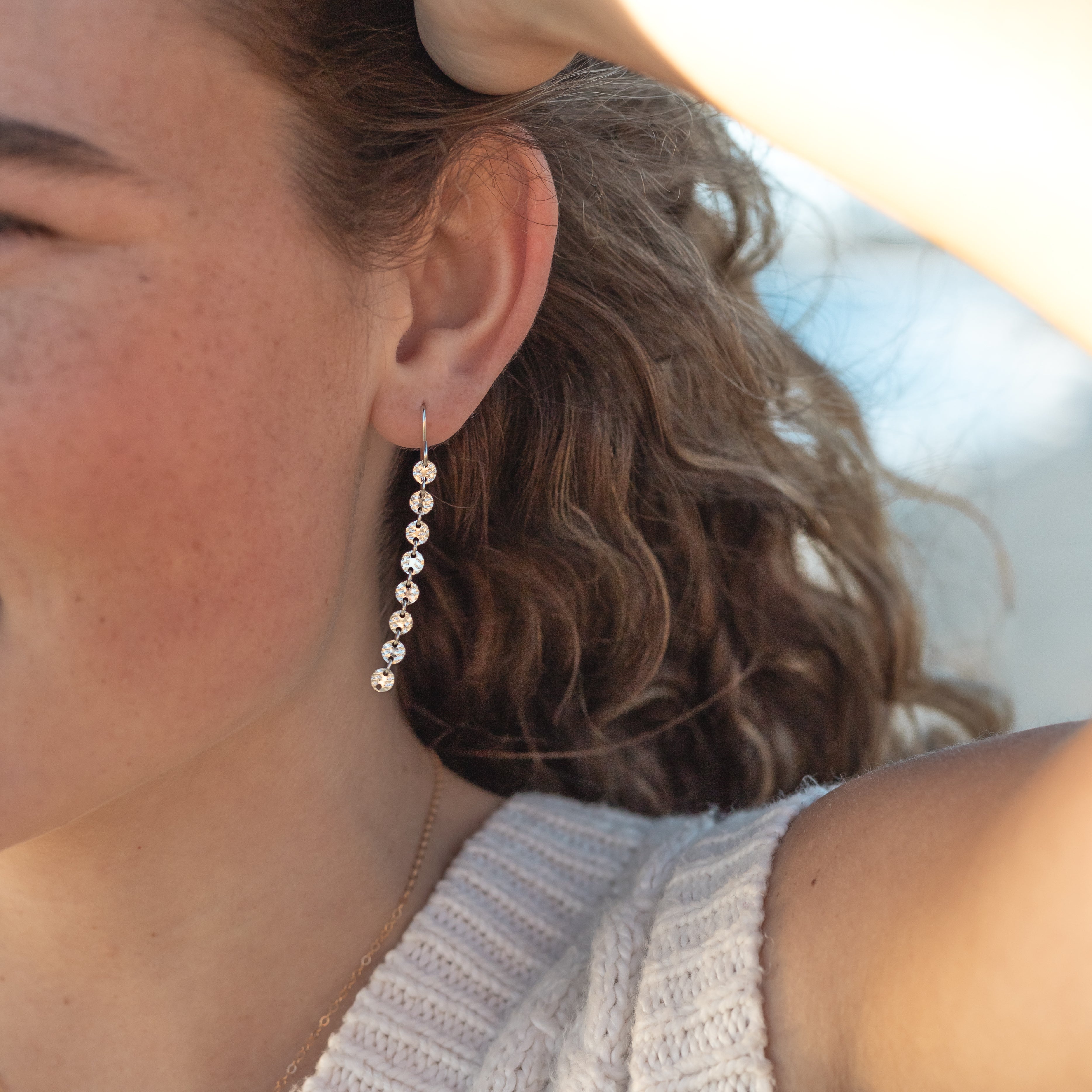 Gold filled dangle disco chain earrings. The chain is tiny circles and the earrings have eight circles hanging. They’re about 2 inches. Shown in a woman’s ear.
