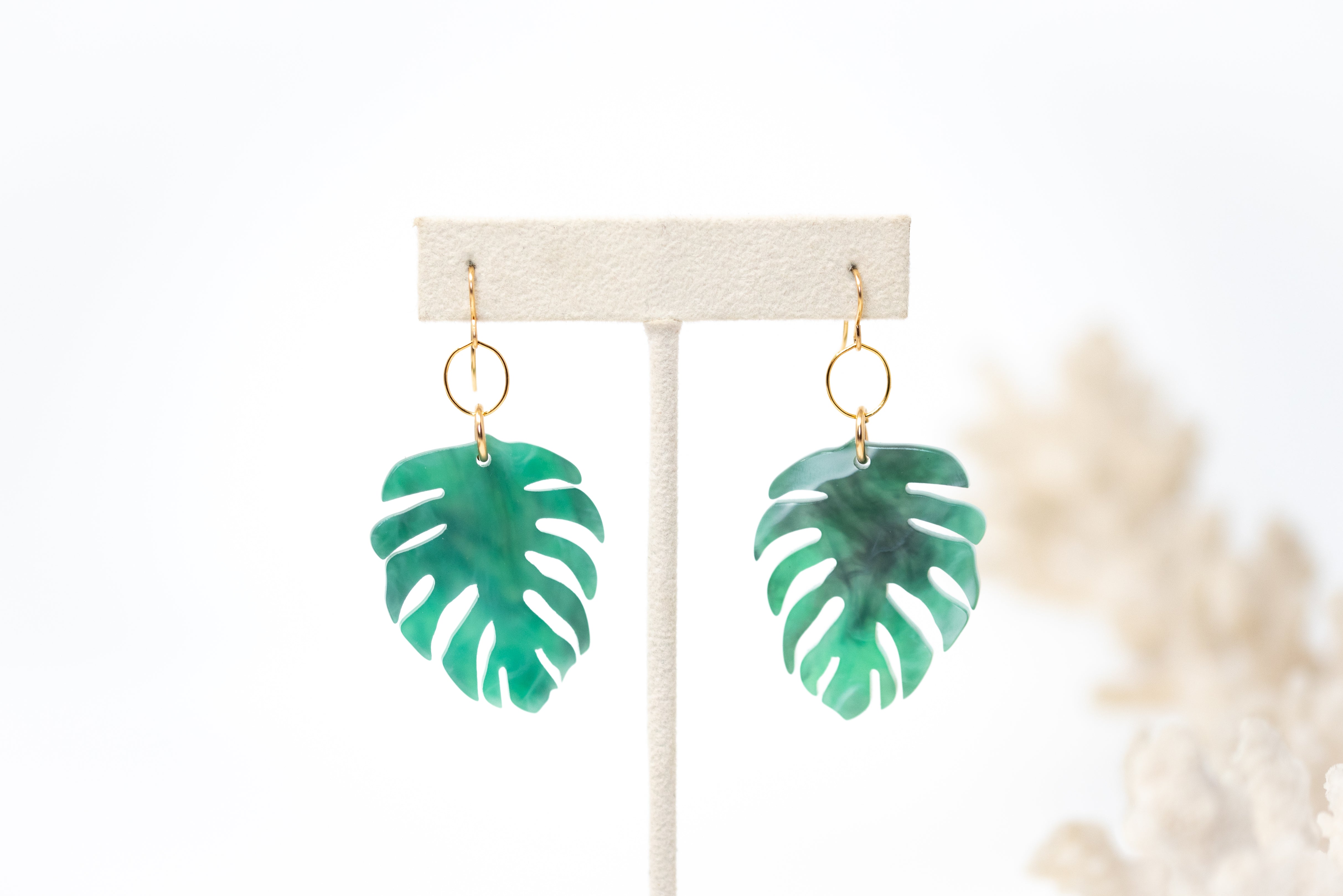Green resin monstera leaf earrings around 1.5 inches long attached to a small gold circle.