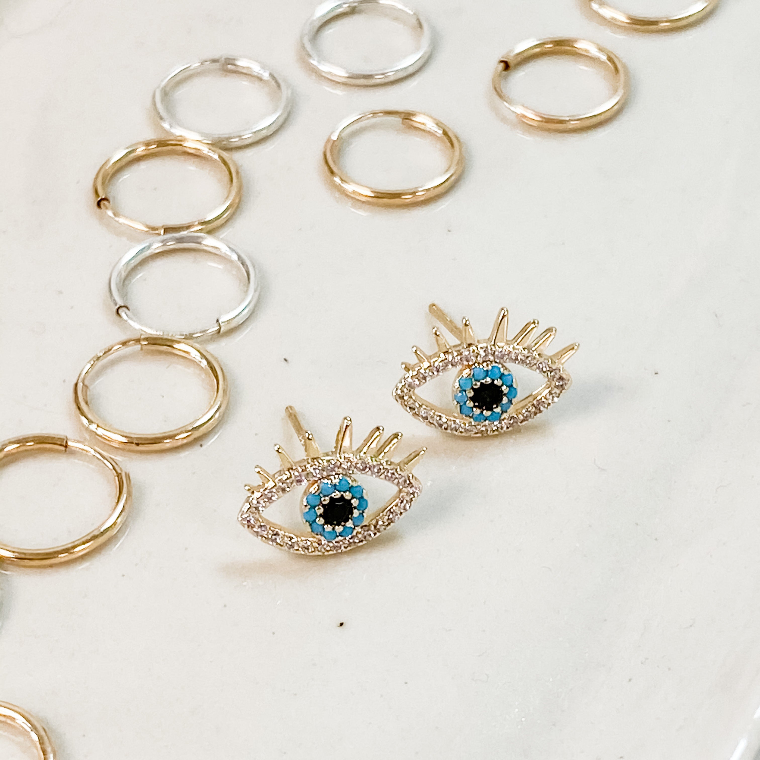 Evil eye stud earrings. Sparkly cubic zirconia and turquoise surrounding the eye. Shown with our second whole small hoops around it.