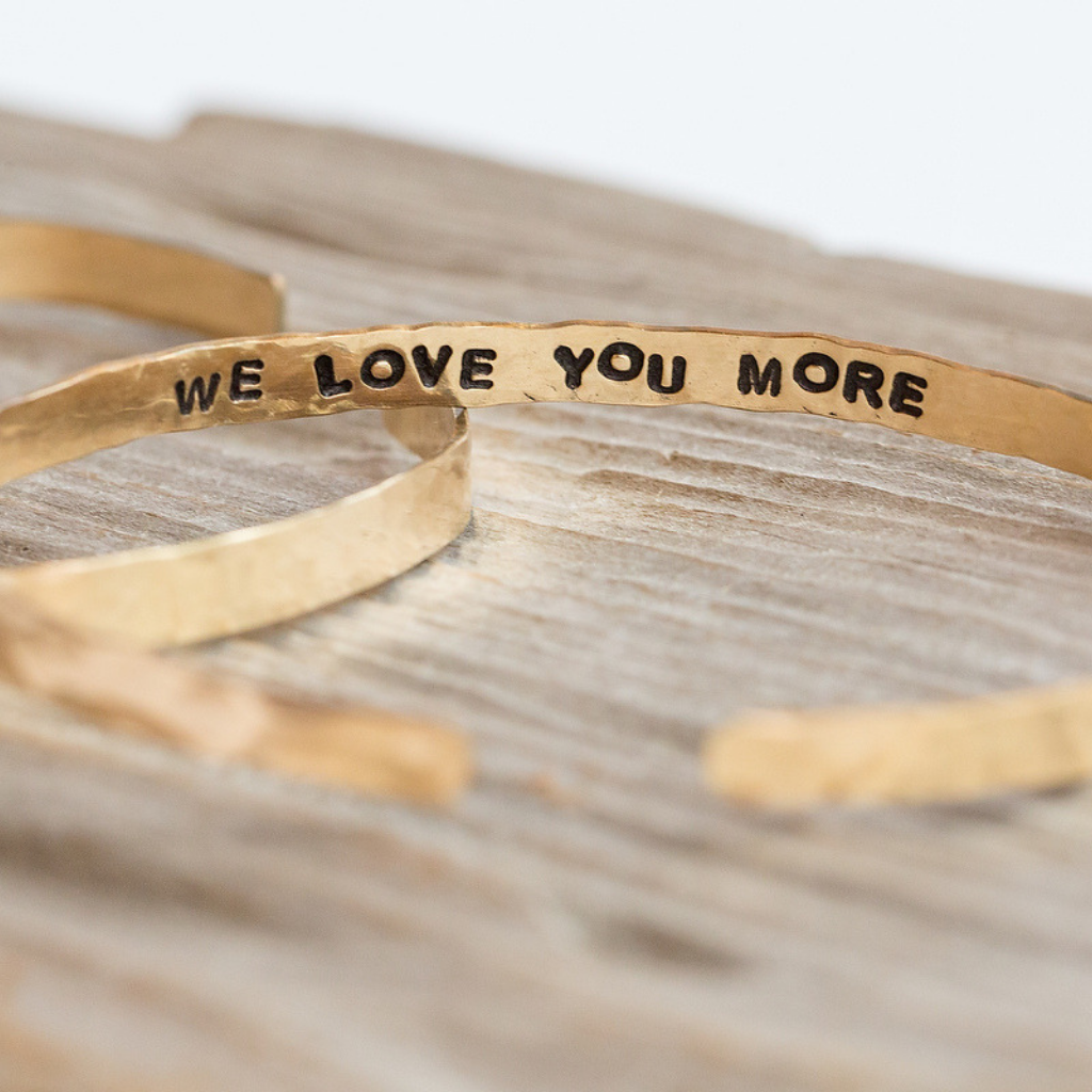 a gold cuff with the phrase "We love you more" stamped on the inside of the cuff. 