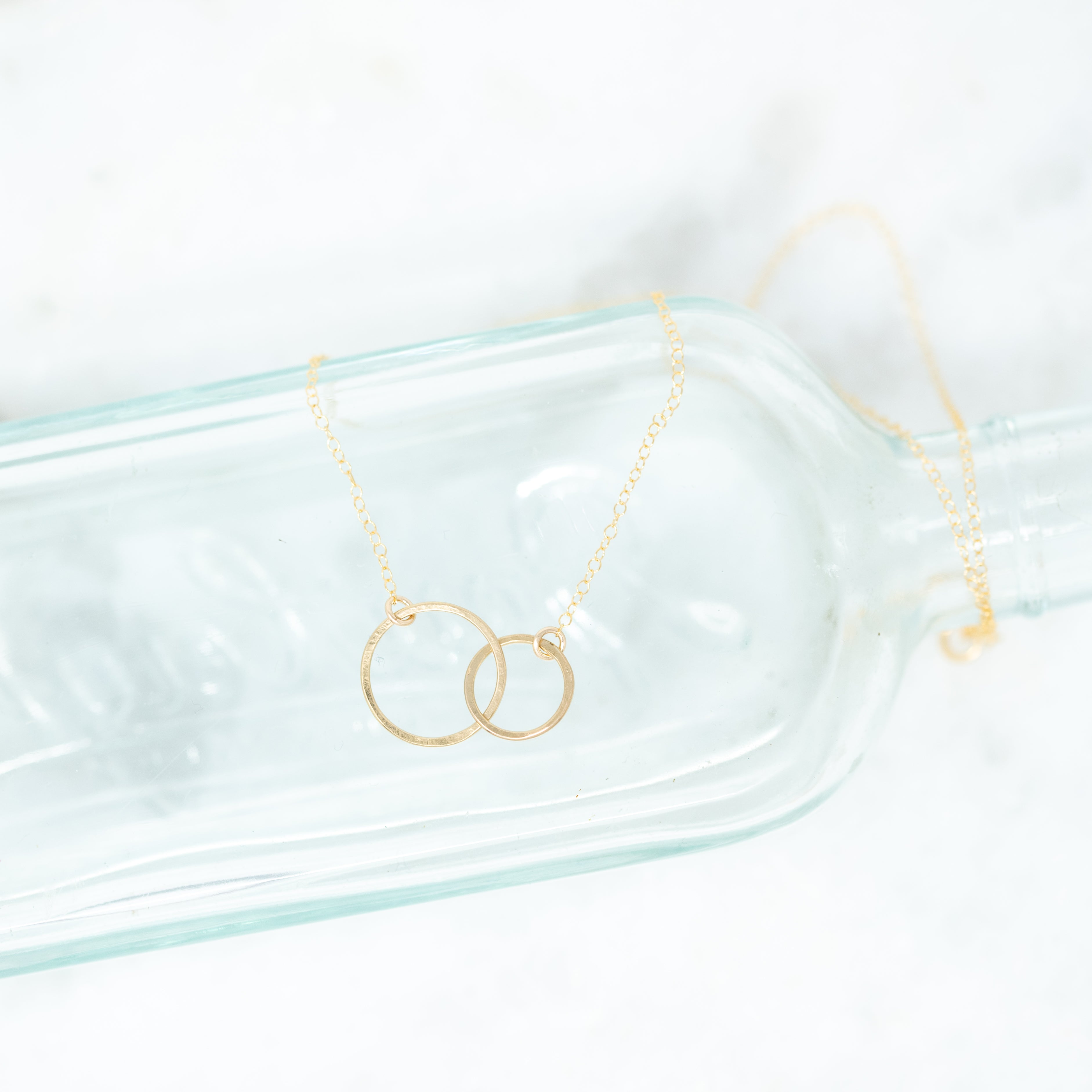 Two gold filled interlocking circles attached to a gold chain. One circle is larger than the other.