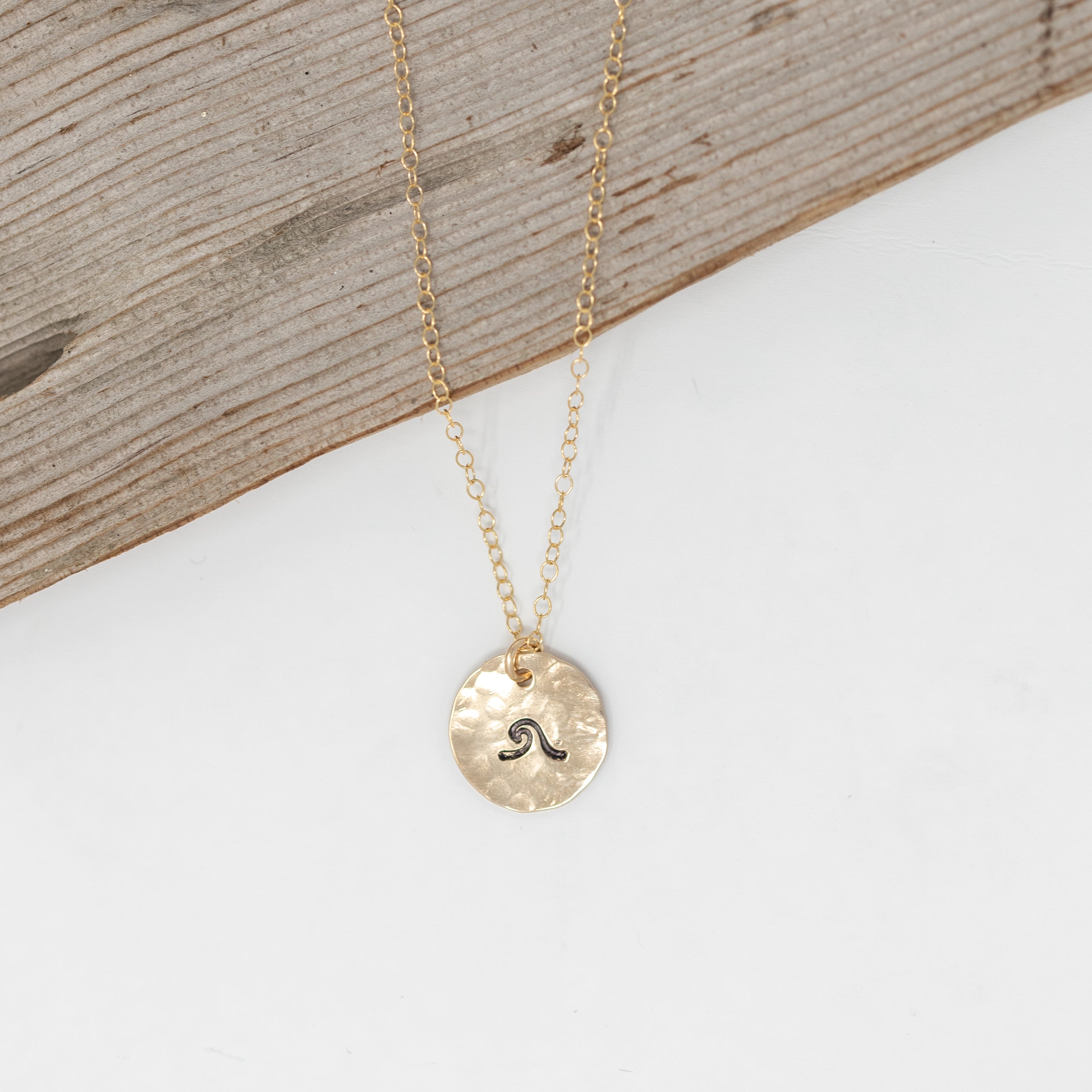 Tiny gold filled circle with a wave stamped onto it. On a gold chain.
