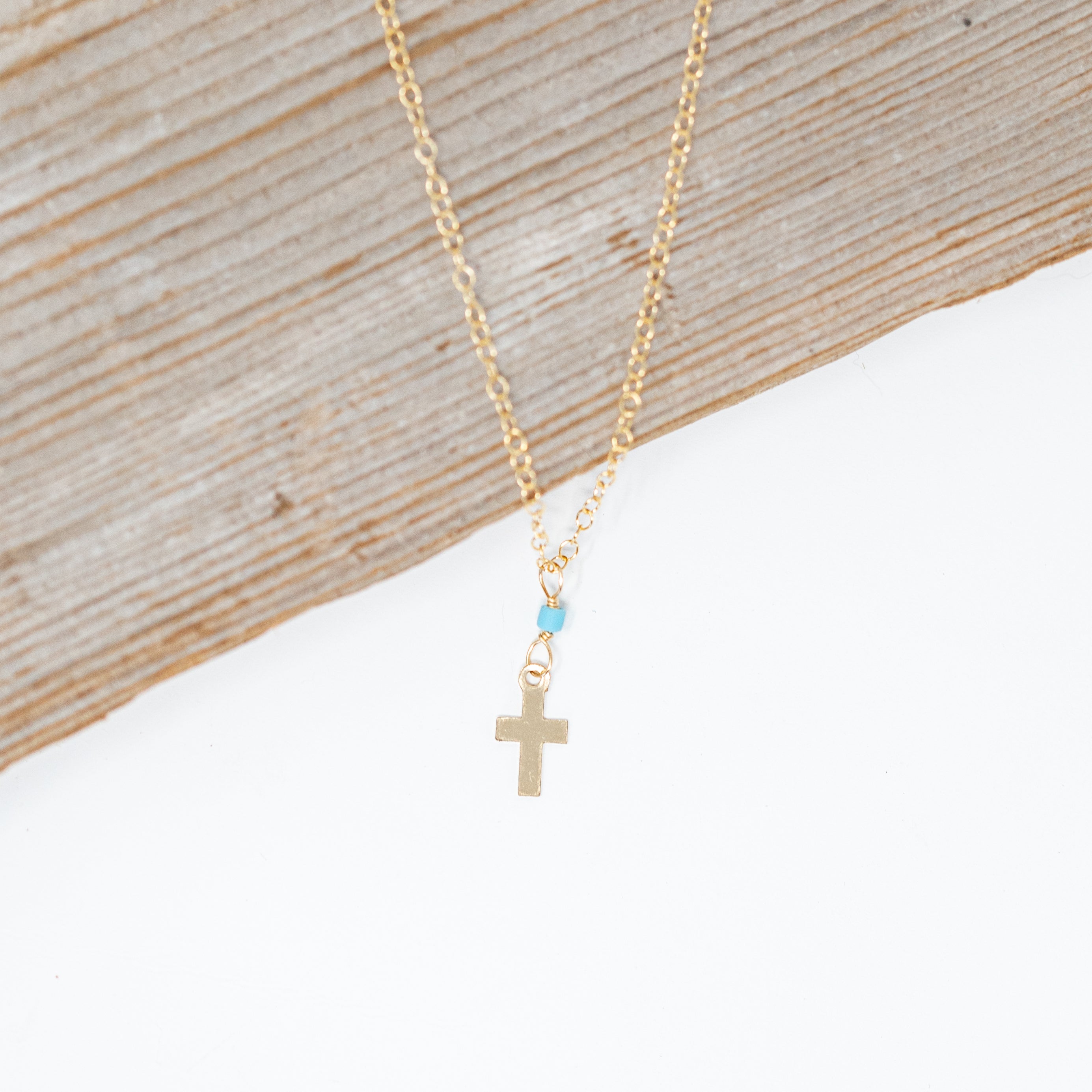 Tiny gold filled cross necklace with a tiny turquoise bead attaching it to a gold chain.