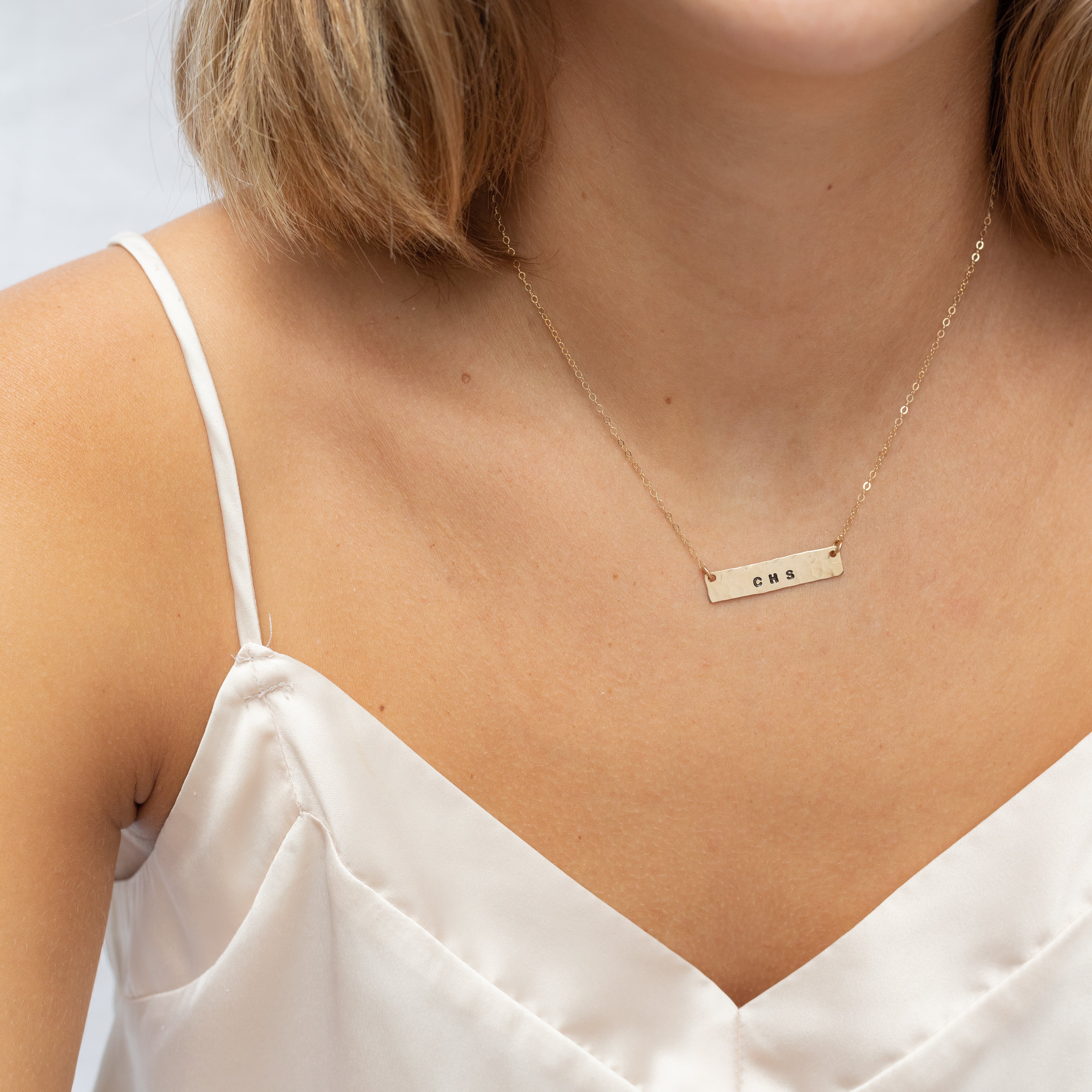 Hand stamped horizontal gold filled bar with phrases on it. Attached to a gold chain. Shown on a woman's neck