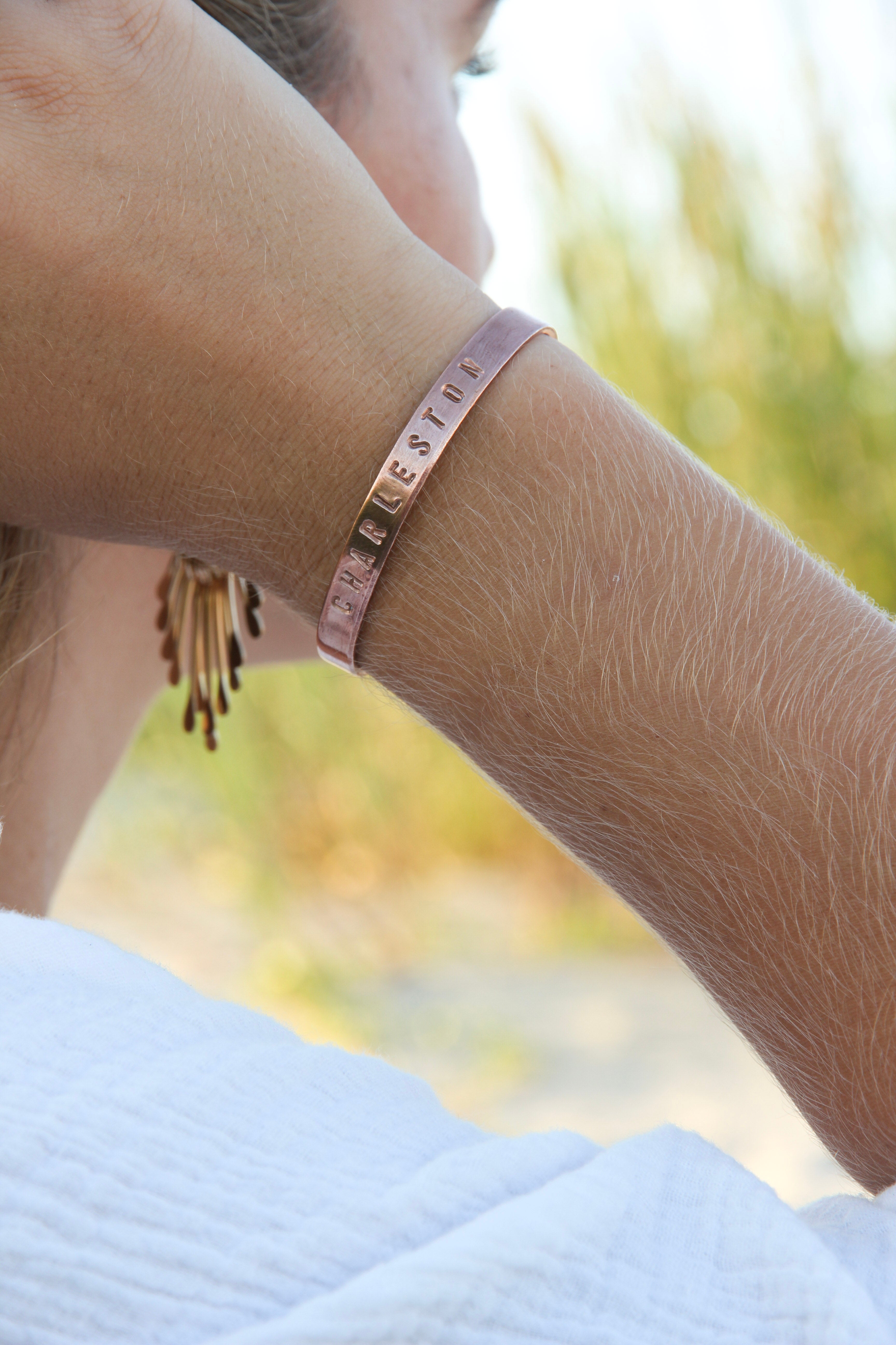 "Charleston" stamped with large letters on the outside of one of our copper cuffs. Shown on a woman's arm. 