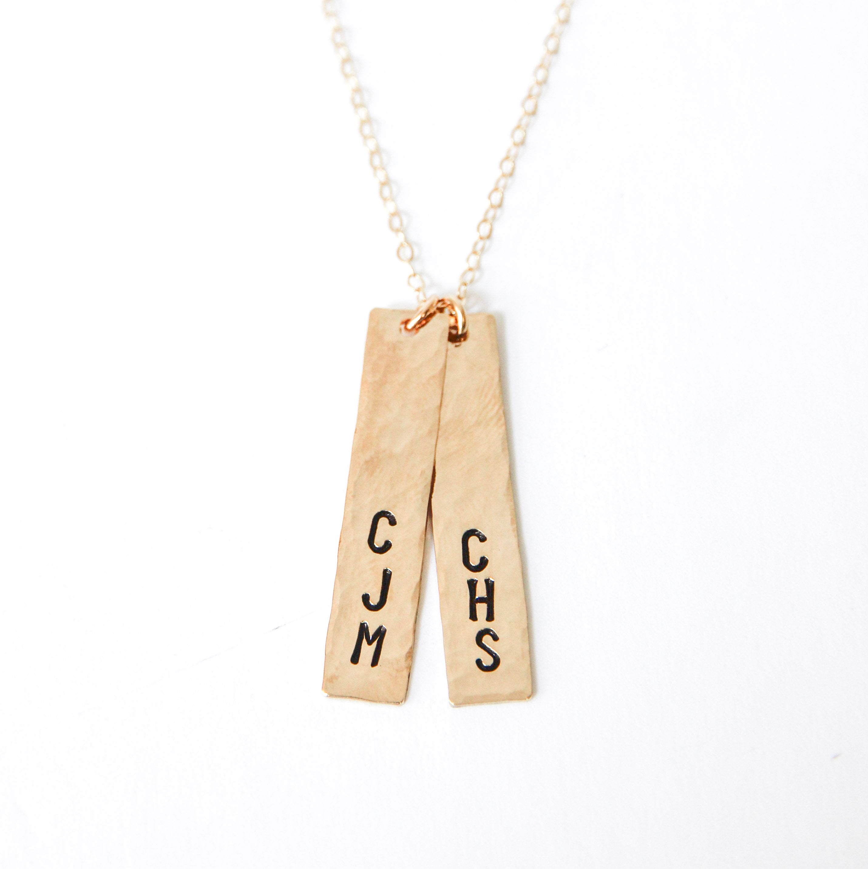 Two vertical gold bar charms with three letter stamped on both of them attached to a gold chain