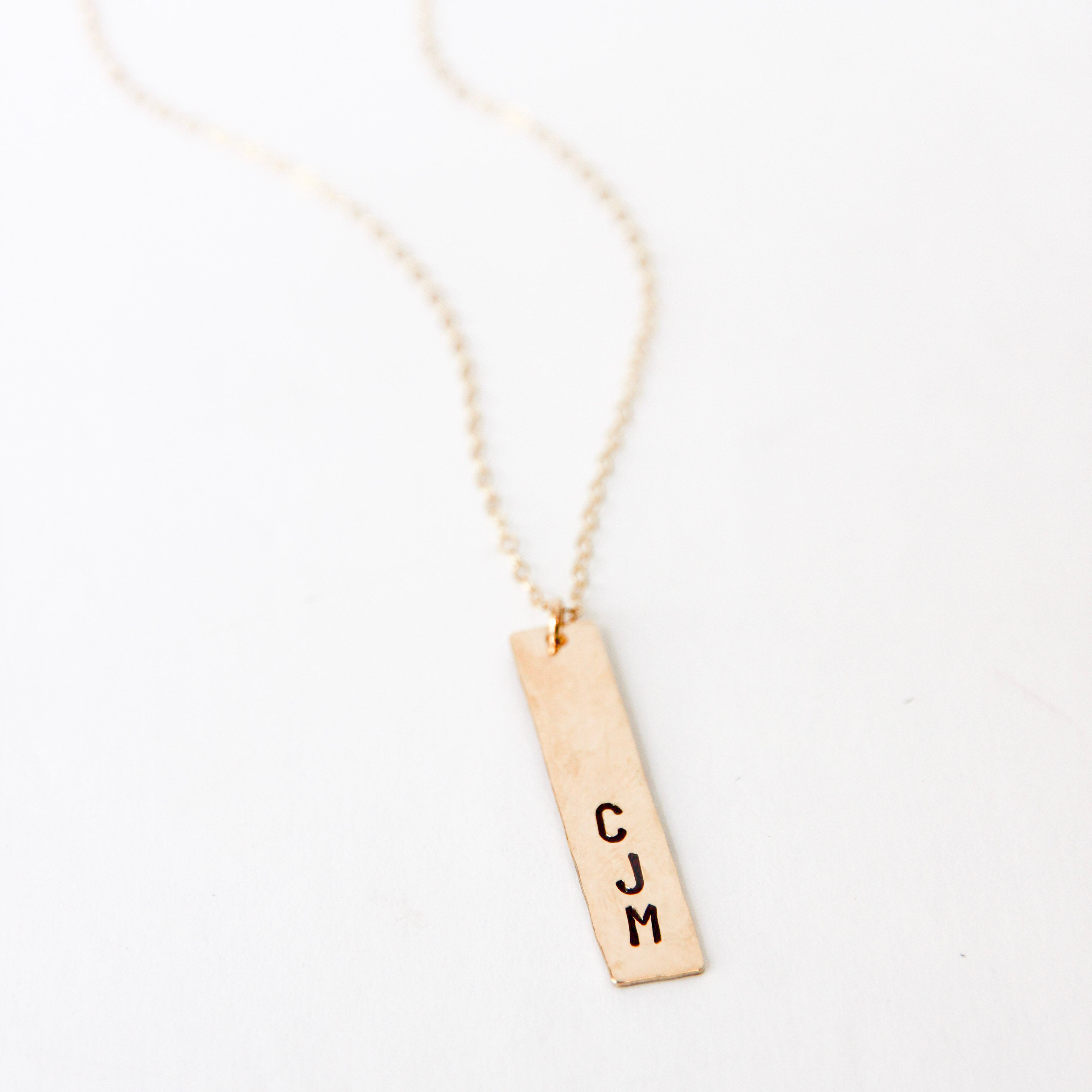 One inch long gold vertical bar with three initials stamped on the end of the bar. Attached to a gold chain. Stamped with the initials CJM