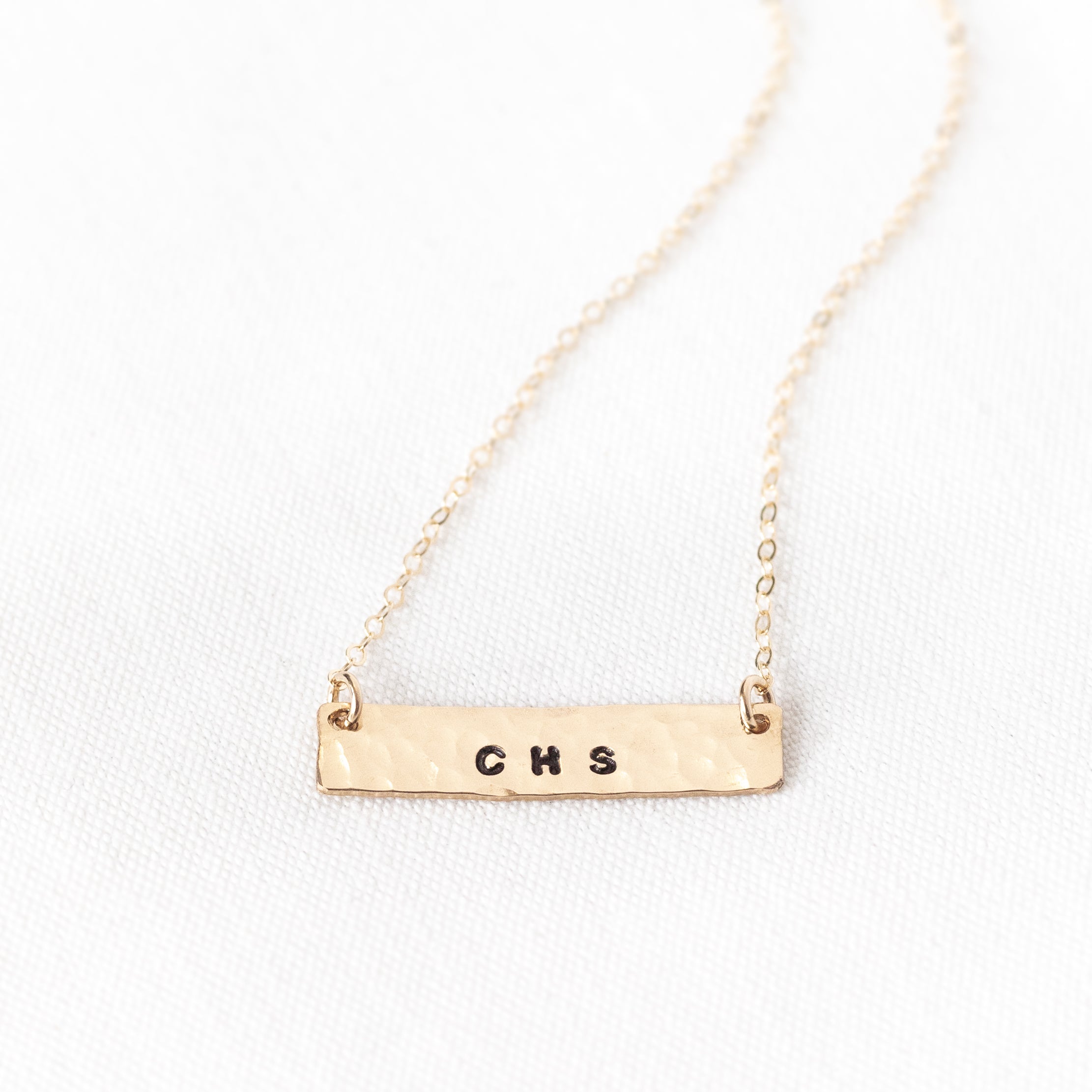 Hand stamped horizontal gold filled bar with phrases on it. Attached to a gold chain. 