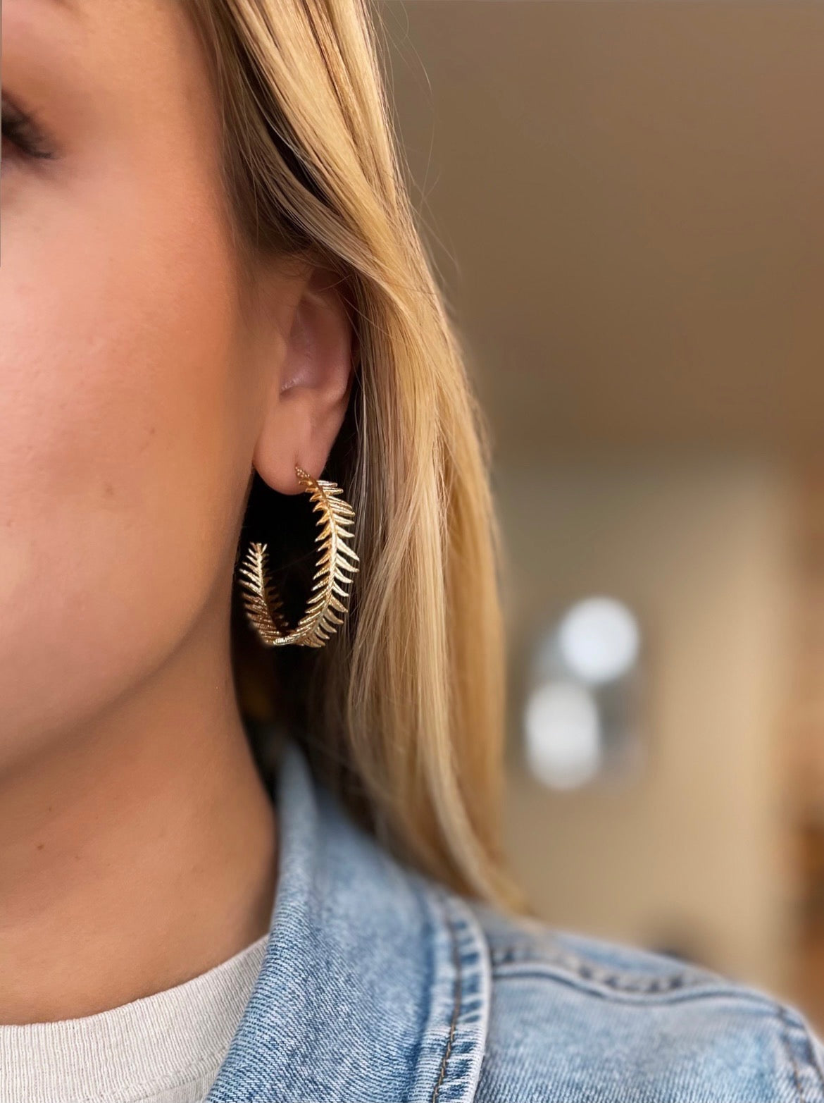 gold plated feather hoop earrings in a woman's ear