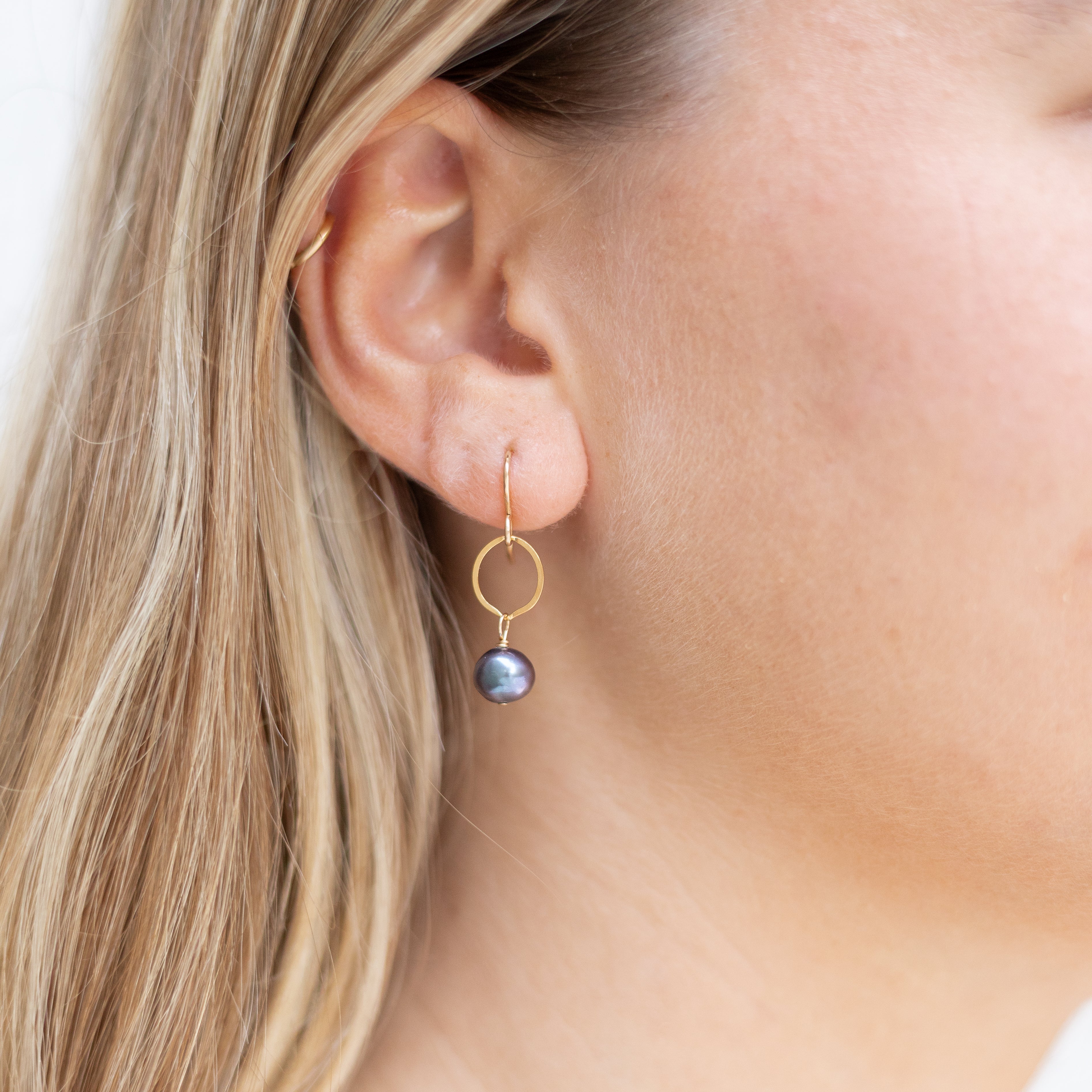Gold filled circles with small dark pearl dangling. Shown in a woman’s ear. 