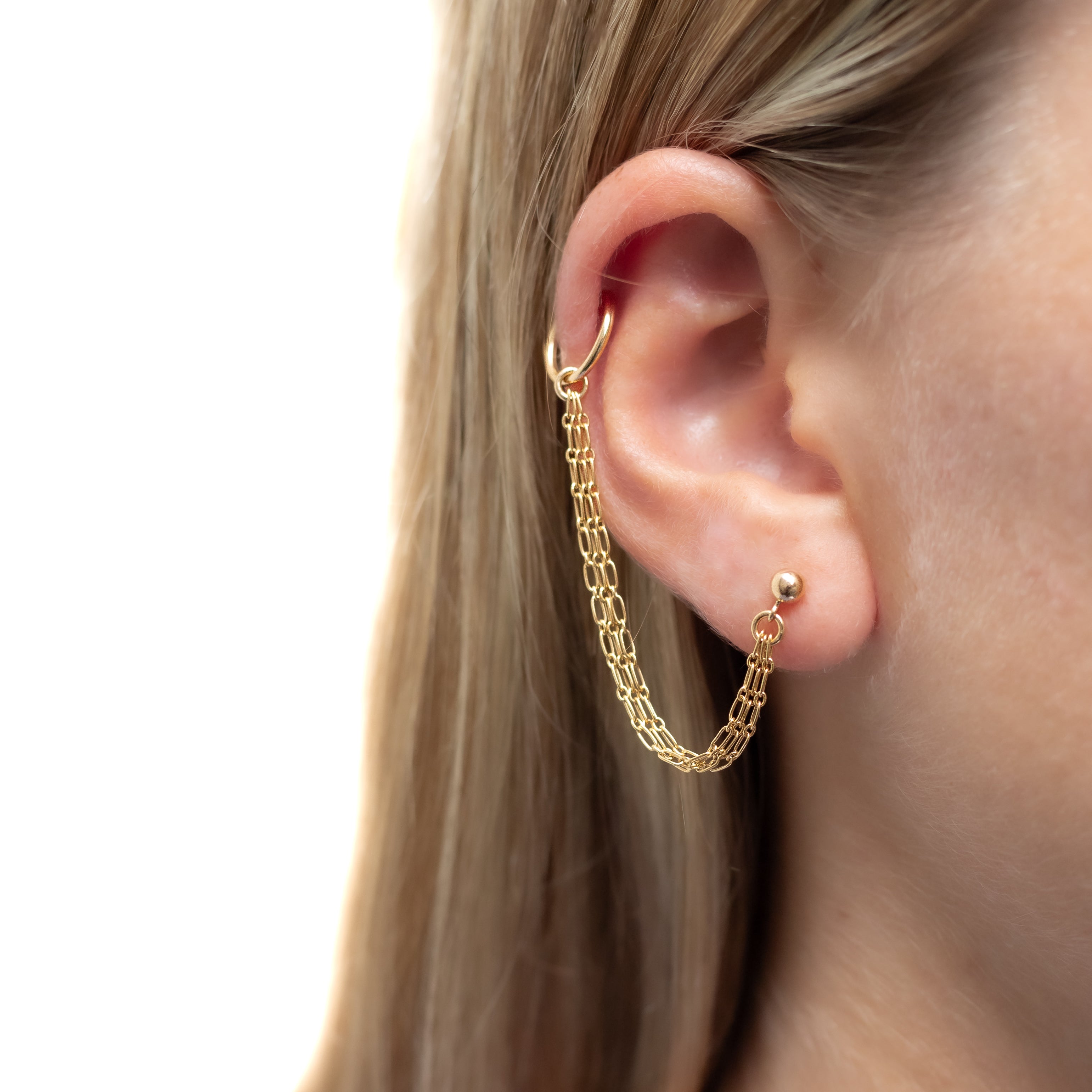 An earring with a gold ball stud in first ear piercing and a huggie hoop in cartilage piercing connected by 3 strands gold chain