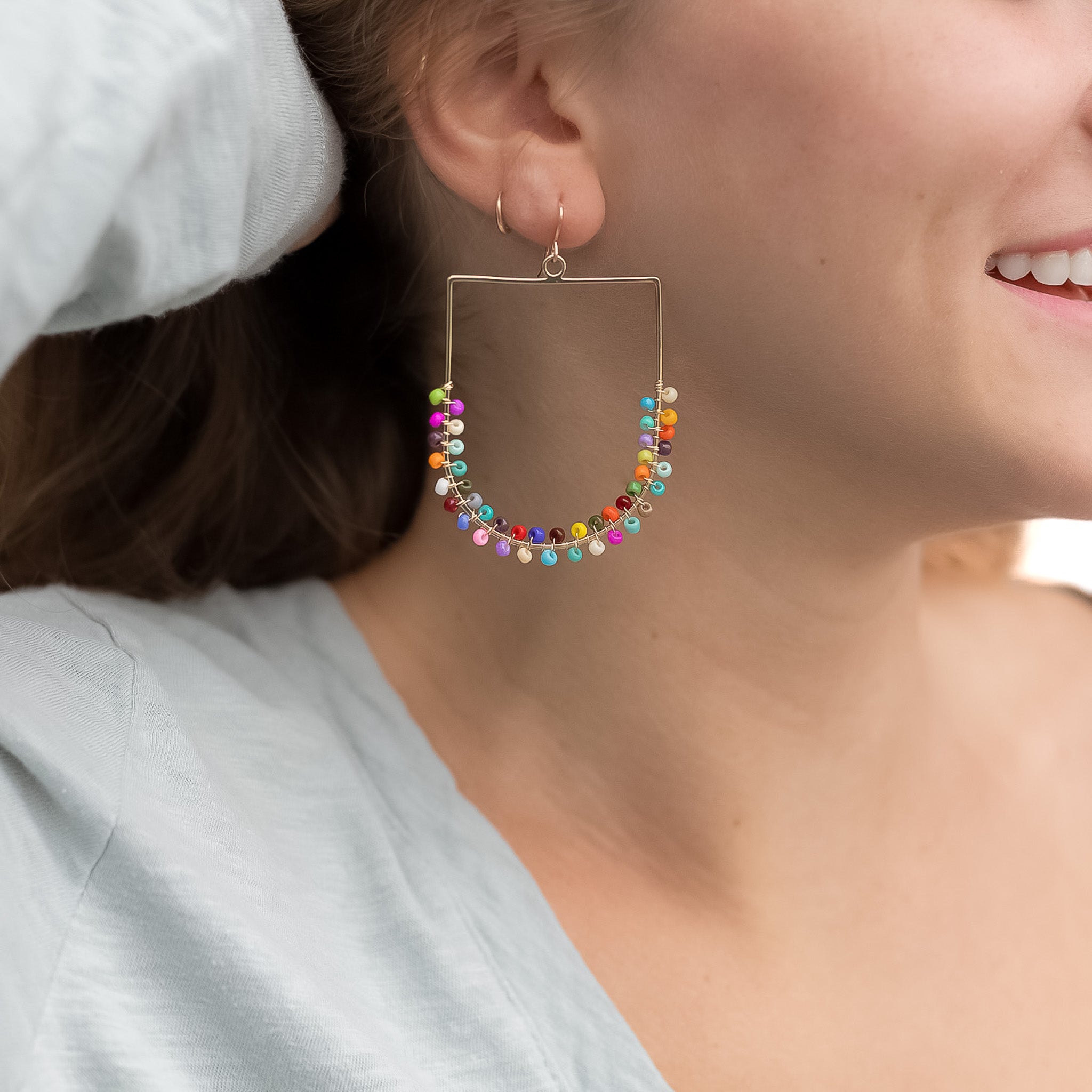 Gold rectangular earings with a curve on the bottom. Wrapped randomly with colorful beads filling the earrings halfway.