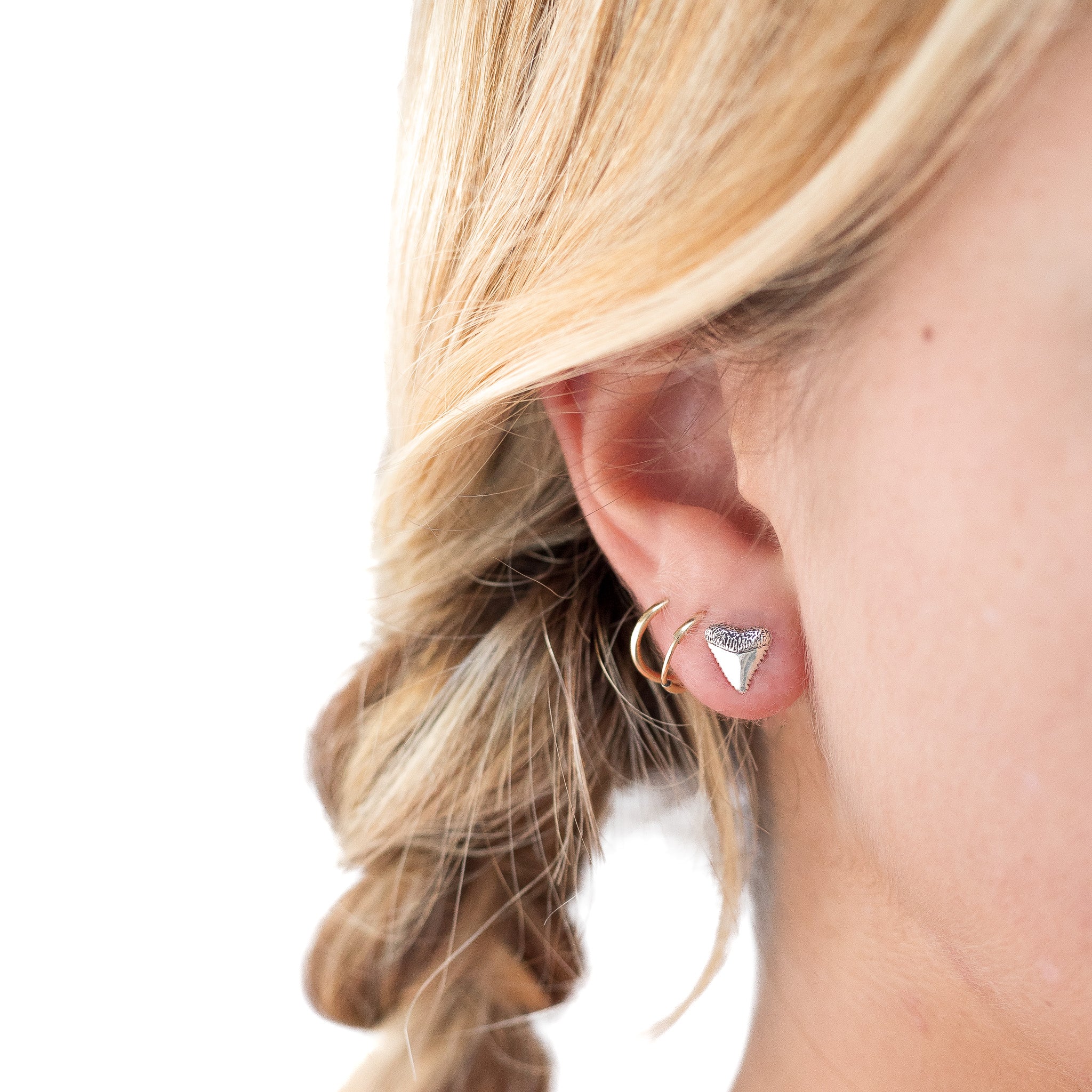 Sterling silver shark tooth stud earrings. Shown on a woman's ear. 