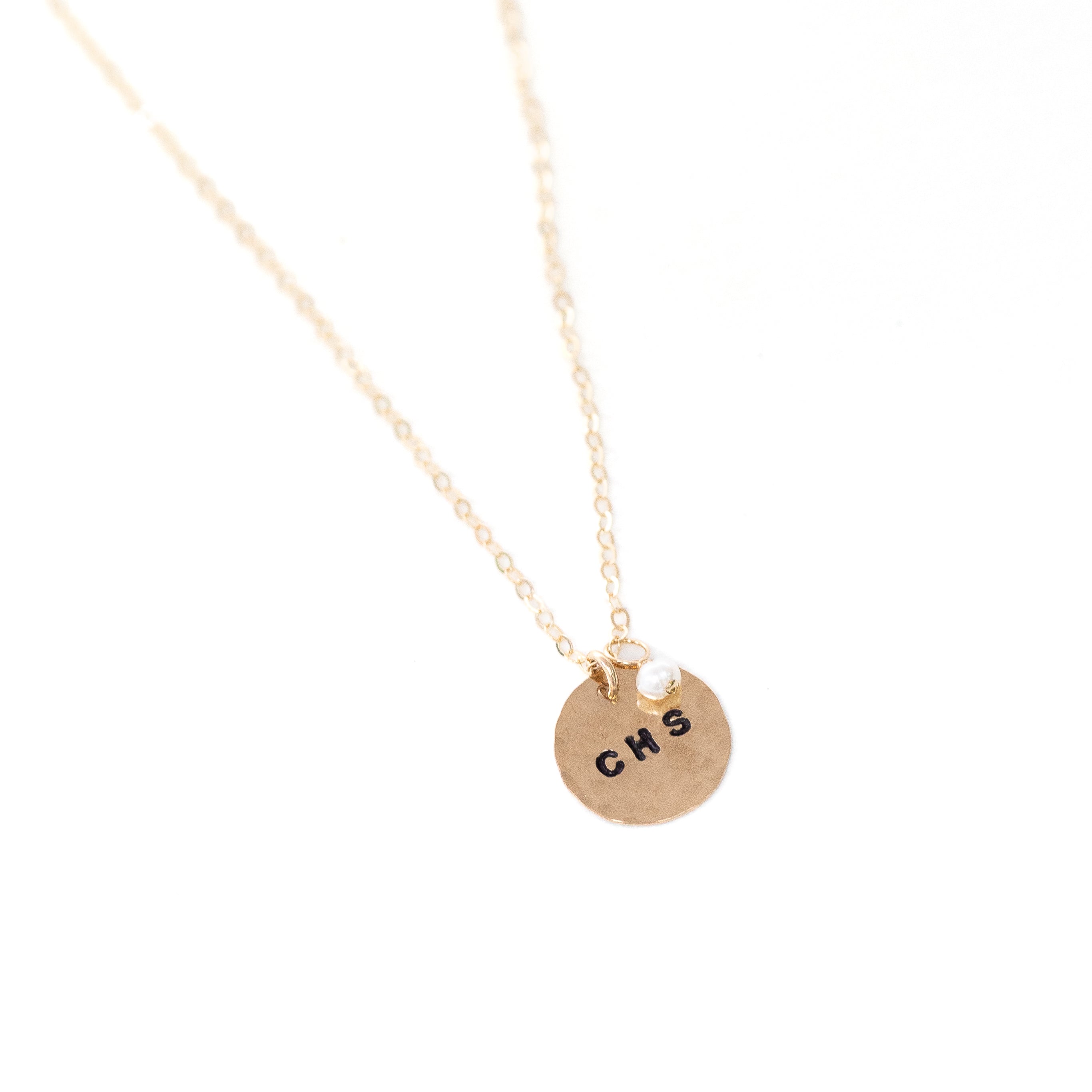 A gold circle stamped necklace with the additional pearl hanging from it.