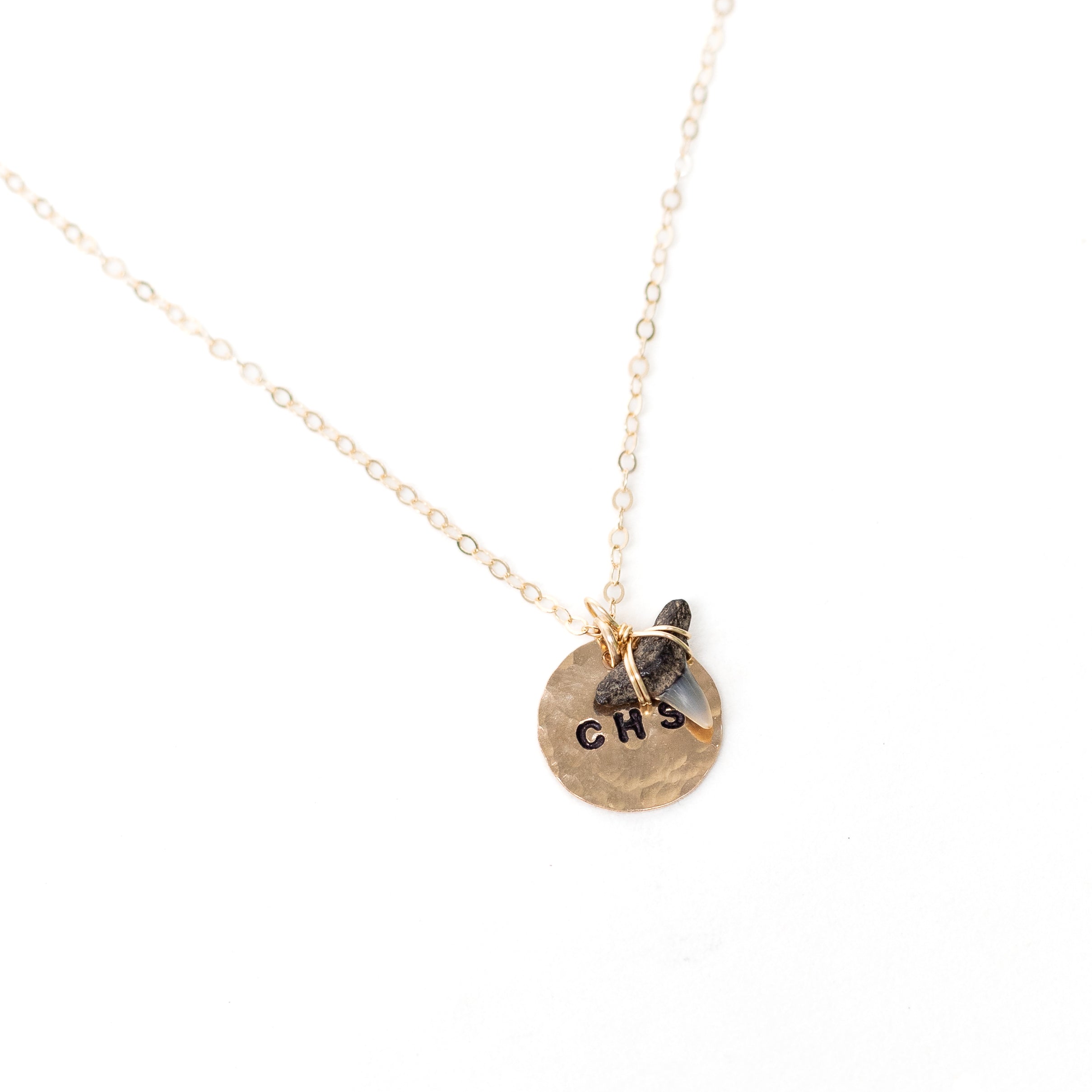 A gold circle stamped necklace with the additional sharks tooth hanging from it.