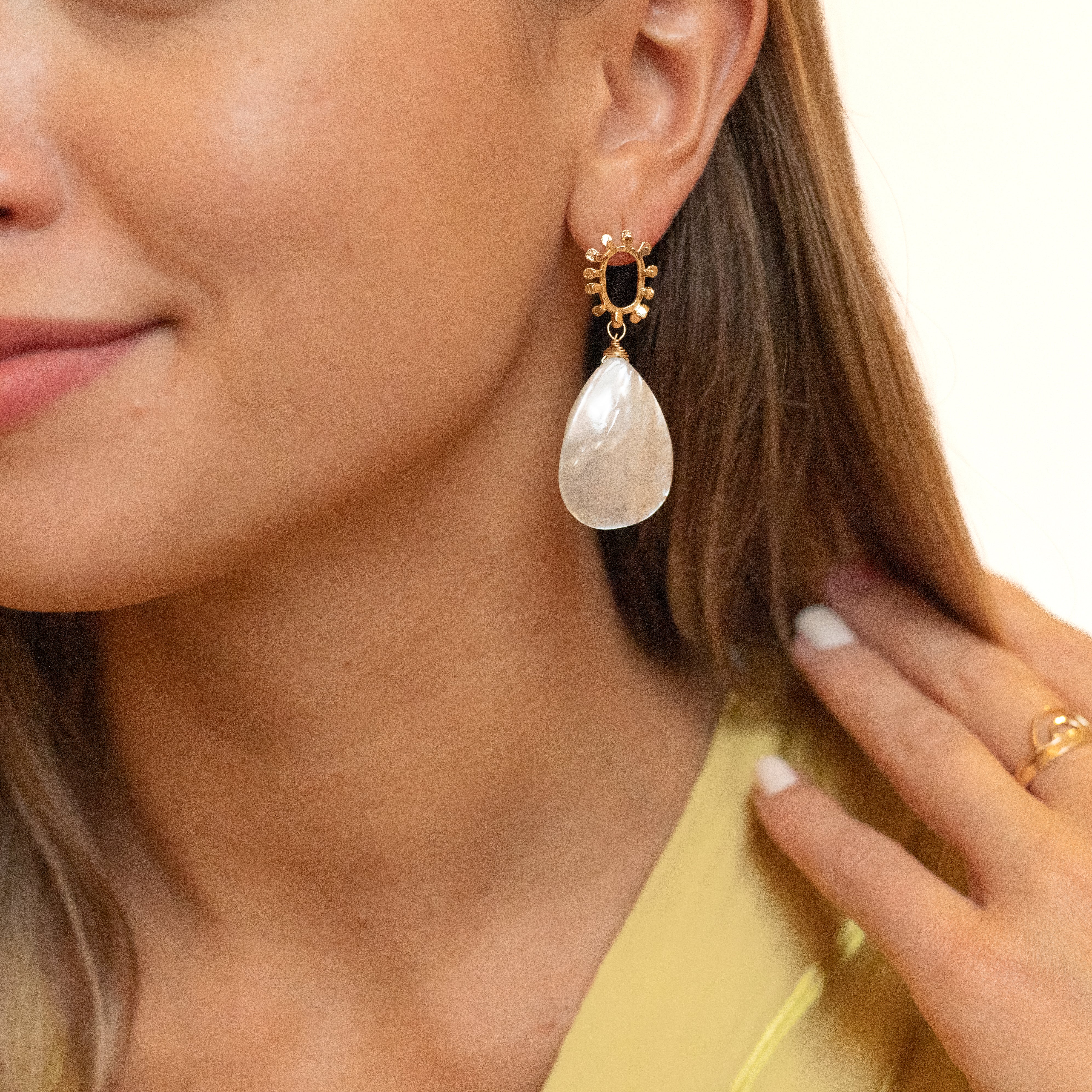 Large mother of pearl tear drops on a dotted, open-circle, gold-plated stud. Shown in a woman's ear. 