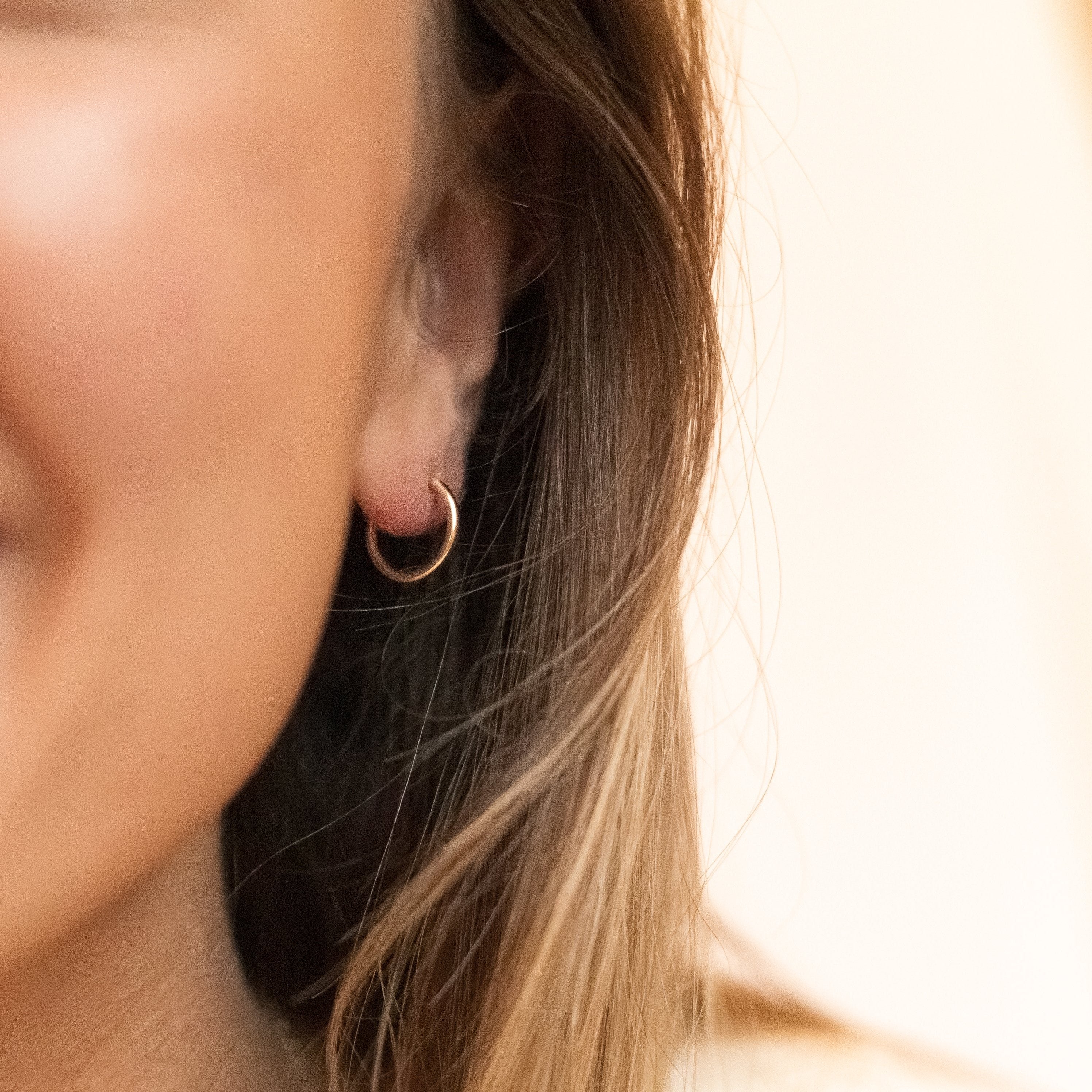 one of the tiny gold filled hoops shown in a woman's ear.