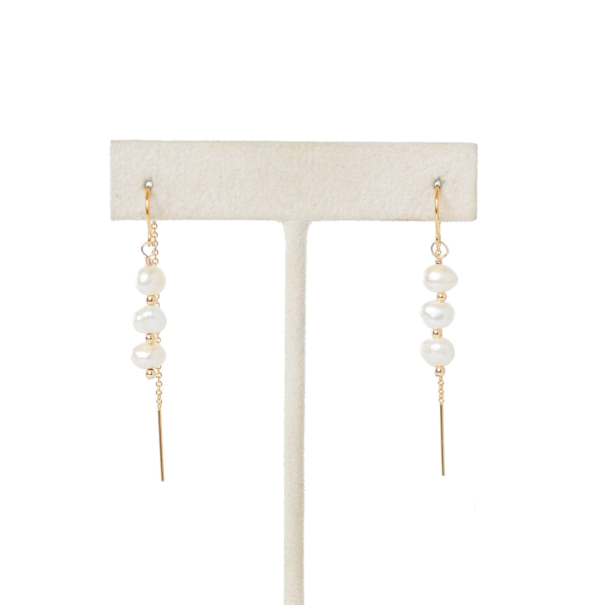 A pair of gold drop earrings with small white pearl beads, displayed on a cream-colored jewelry stand against a solid white background.