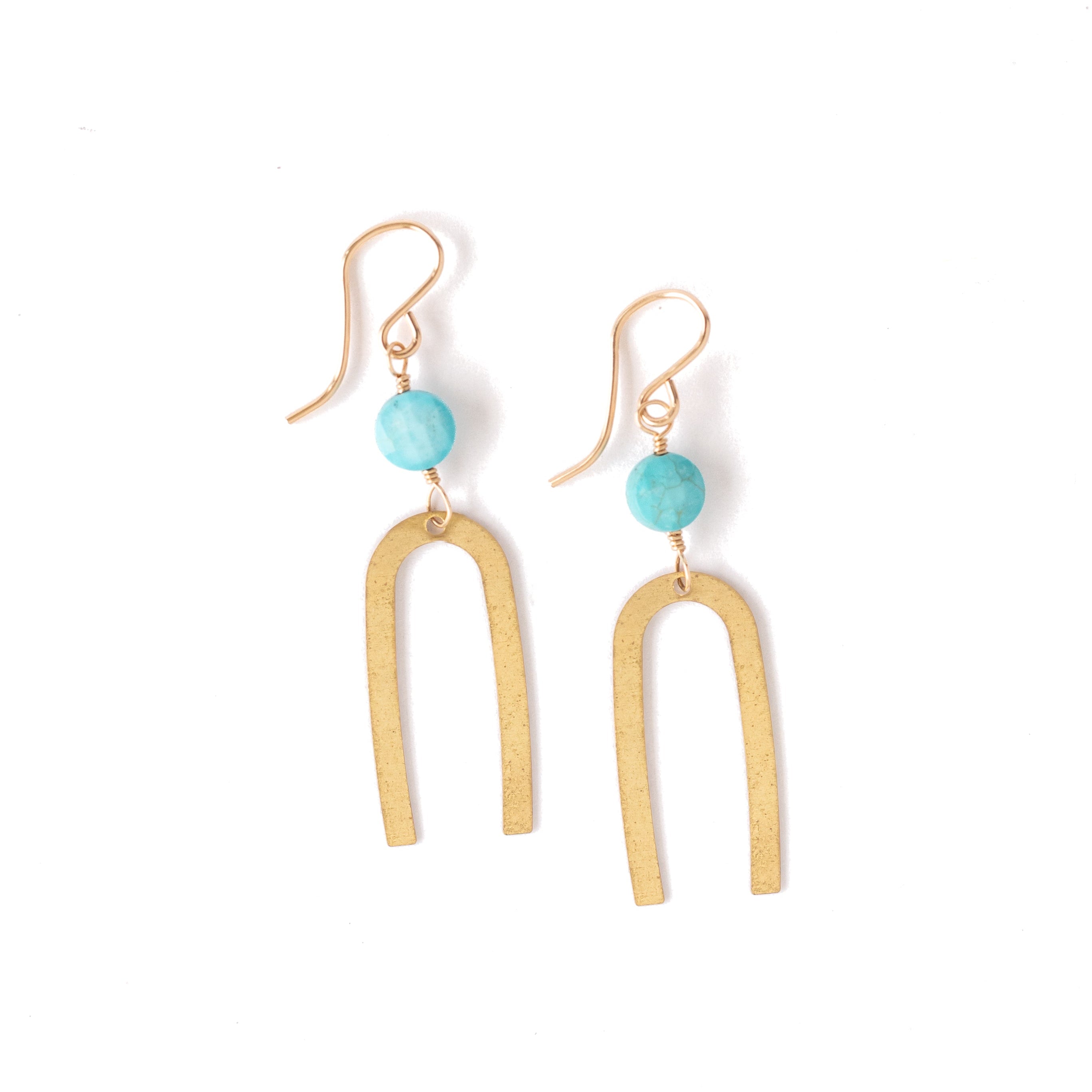 A pair of gold-toned dangle earrings with a small round turquoise bead and a larger abstract U-shaped drop, shown on a plain white background.