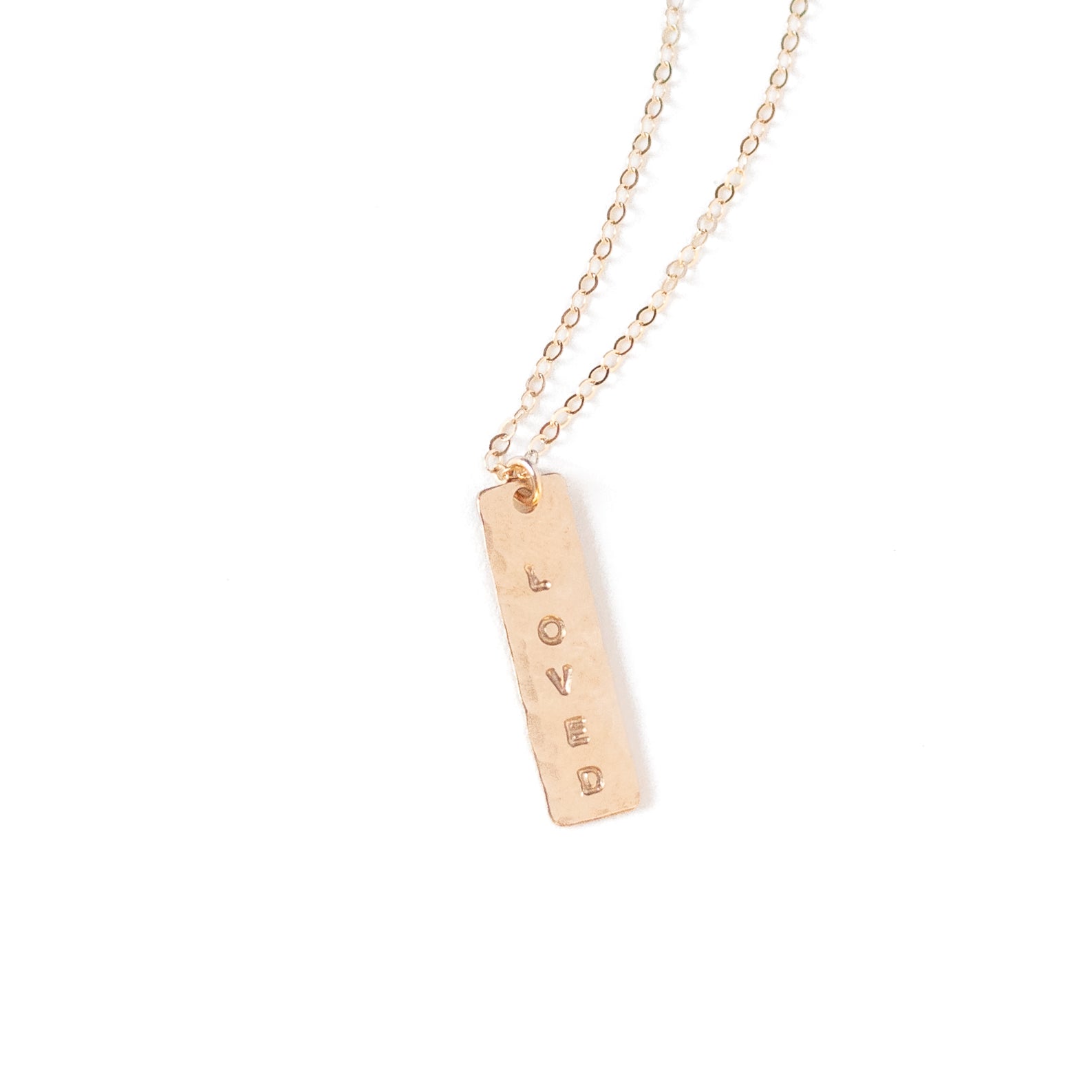 About an inch long vertical gold bar with “Loved” stamped onto it. On our basic gold chain. 