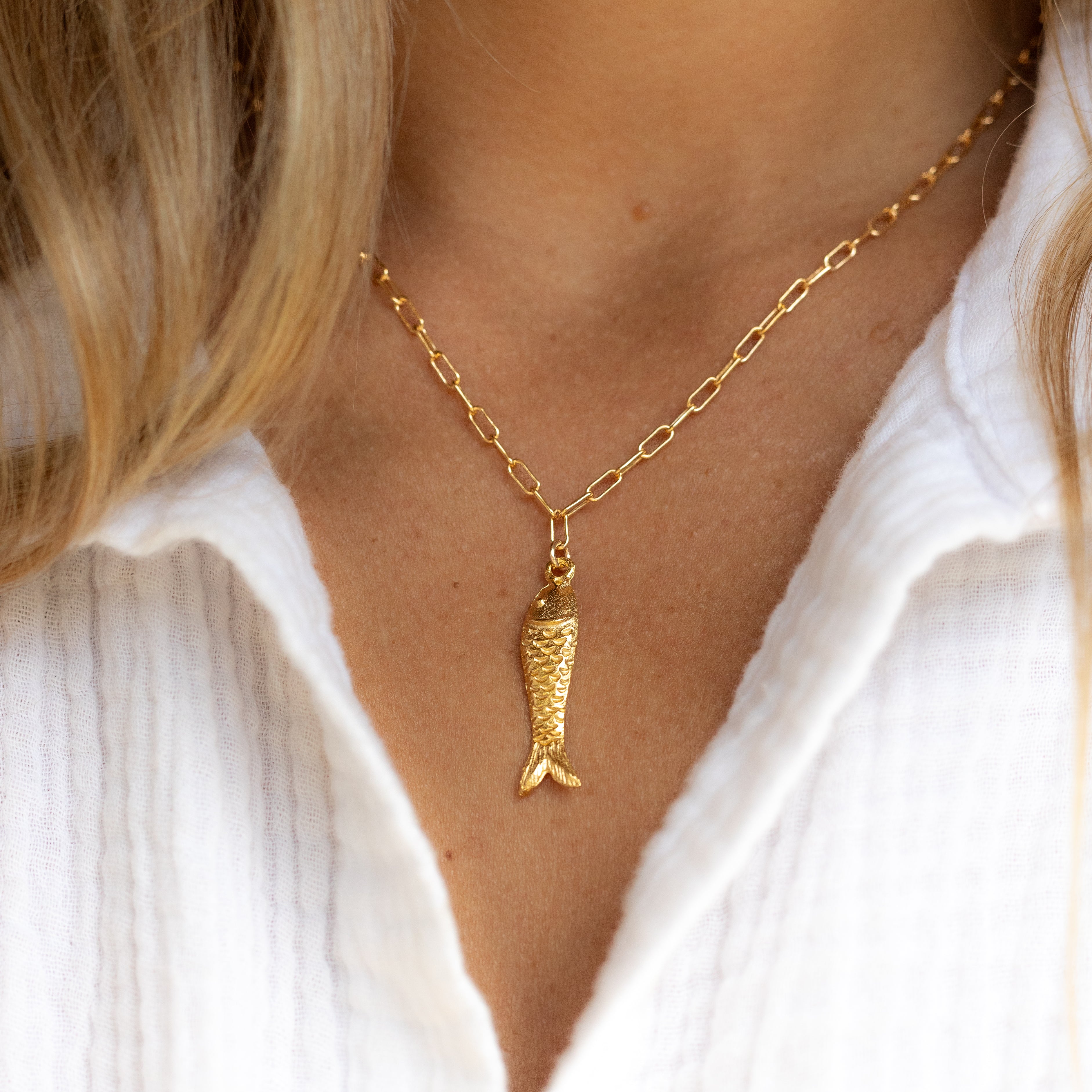 Gold one inch long fish pendant dangling from gold filled paperclip chain. Shown on a woman’s neck. 