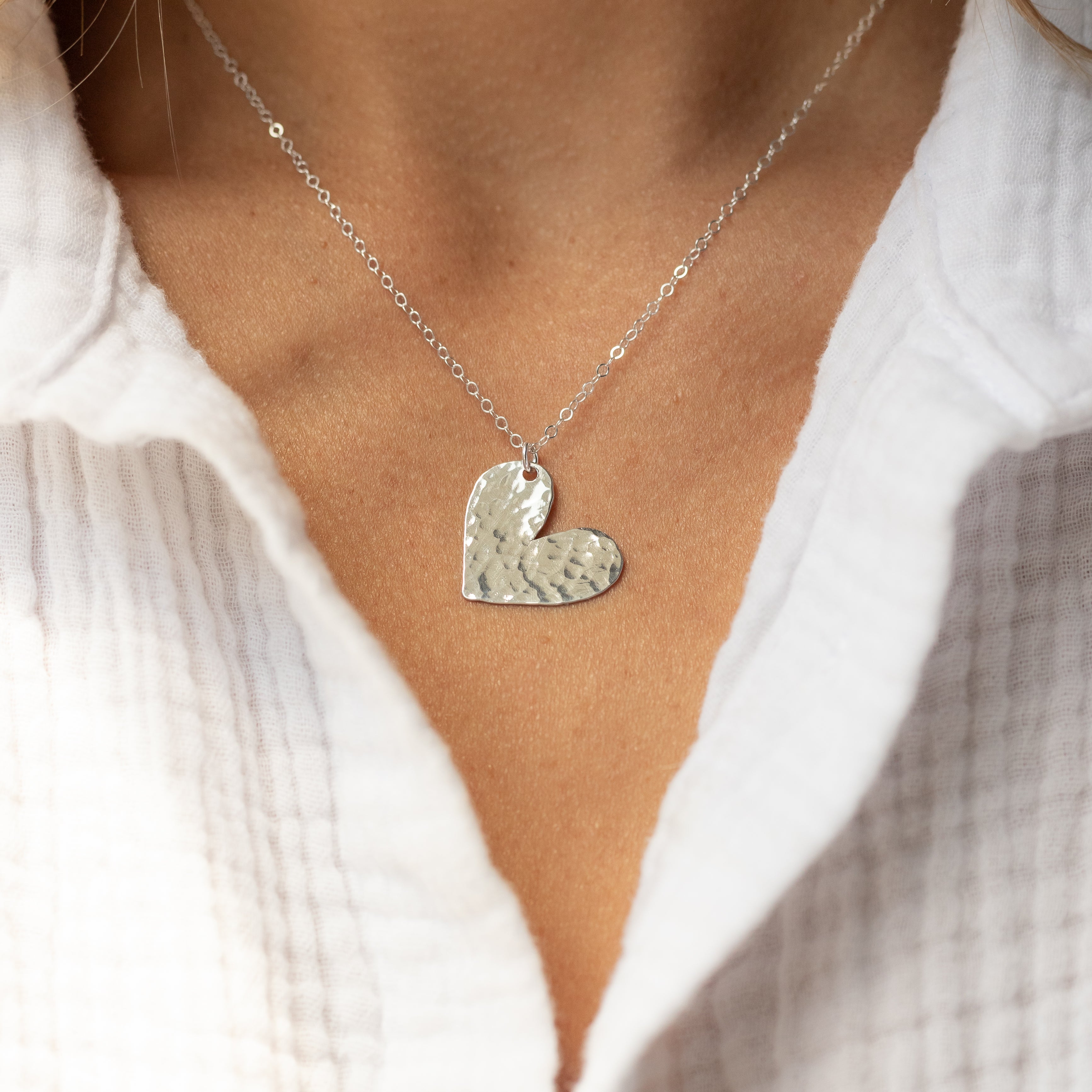 Sterling silver hand cut heart charm nickle-quarter size, attached to a silver chain on a neck. 