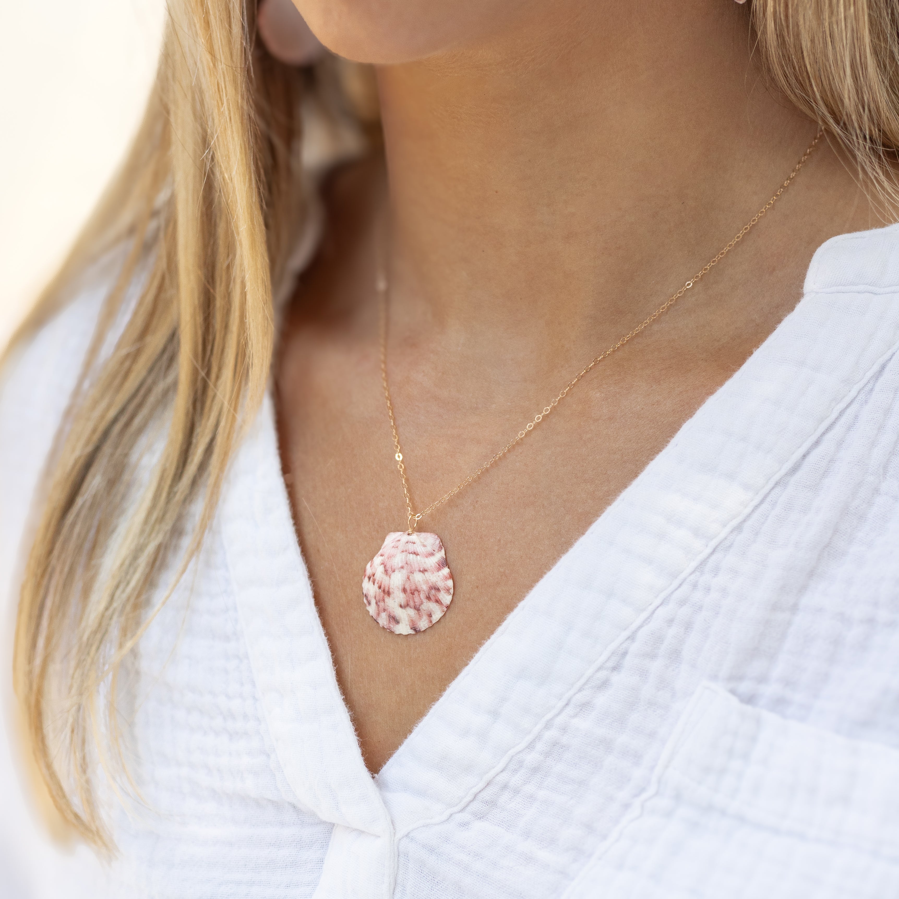 Pink and white seashell shown on our basic gold chain on a woman’s neck. 