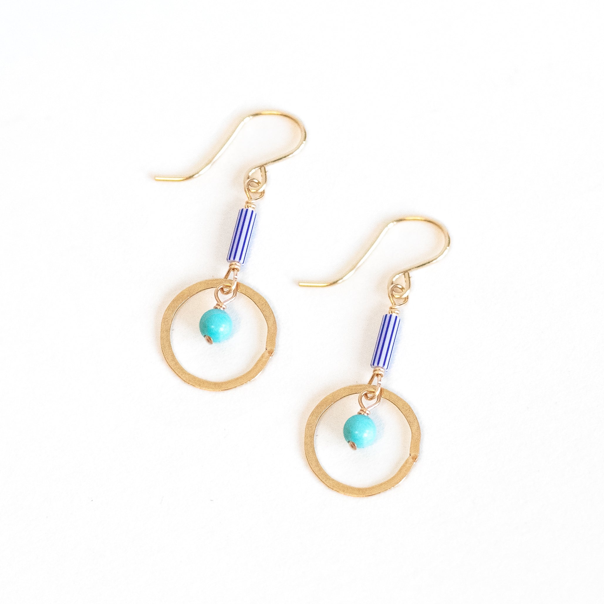 Earrings with a Blue and white striped bead from Ghana wire wrapped to a gold circle and turquoise bead inside the gold circle. 