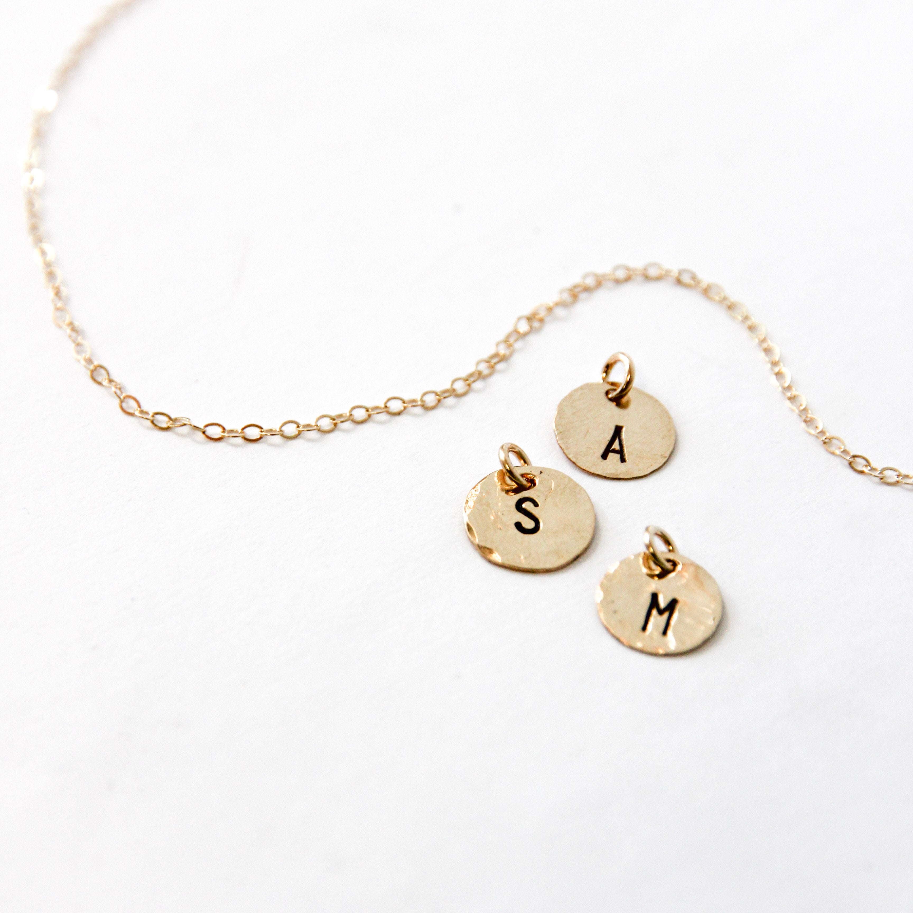 Three tiny single initial stamped gold circles. With letter A, S and M showing. Our basic gold chain is behind it 