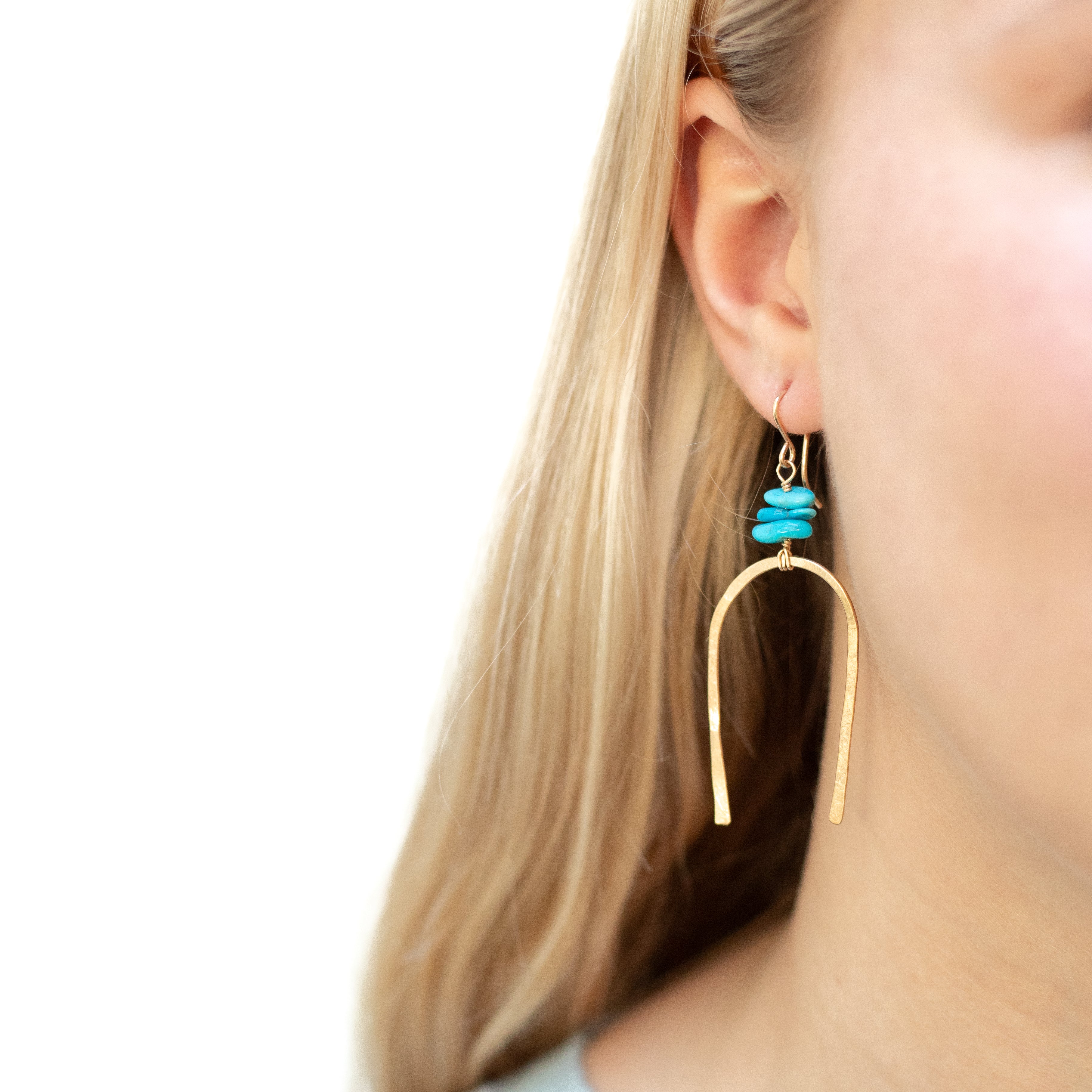 Gold filled large horseshoe with three turquoise beads wire wrapped above it. Shown in a woman’s ear. 