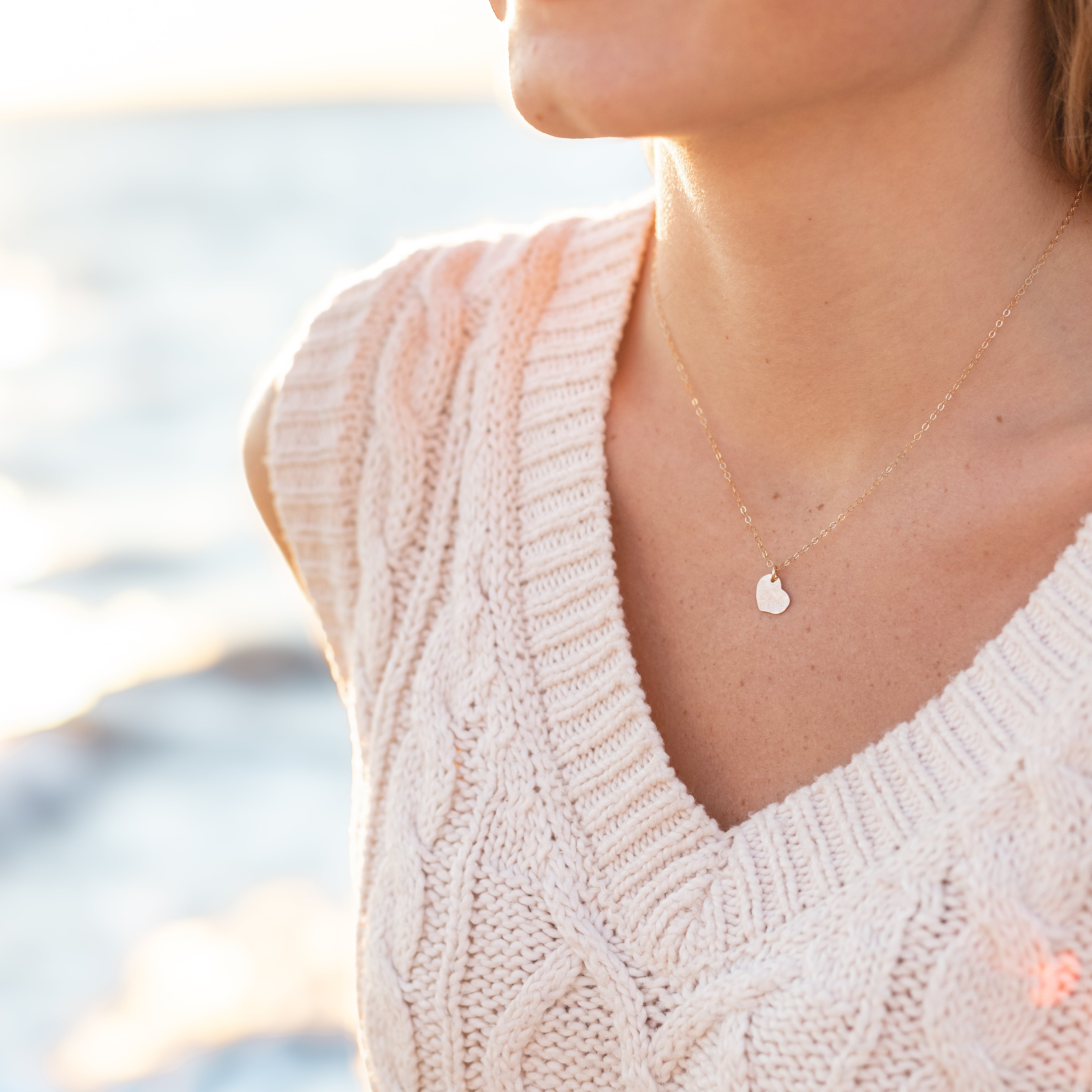 Tiny Rose gold heart on a gold chain. Shown on a woman’s neck. 
