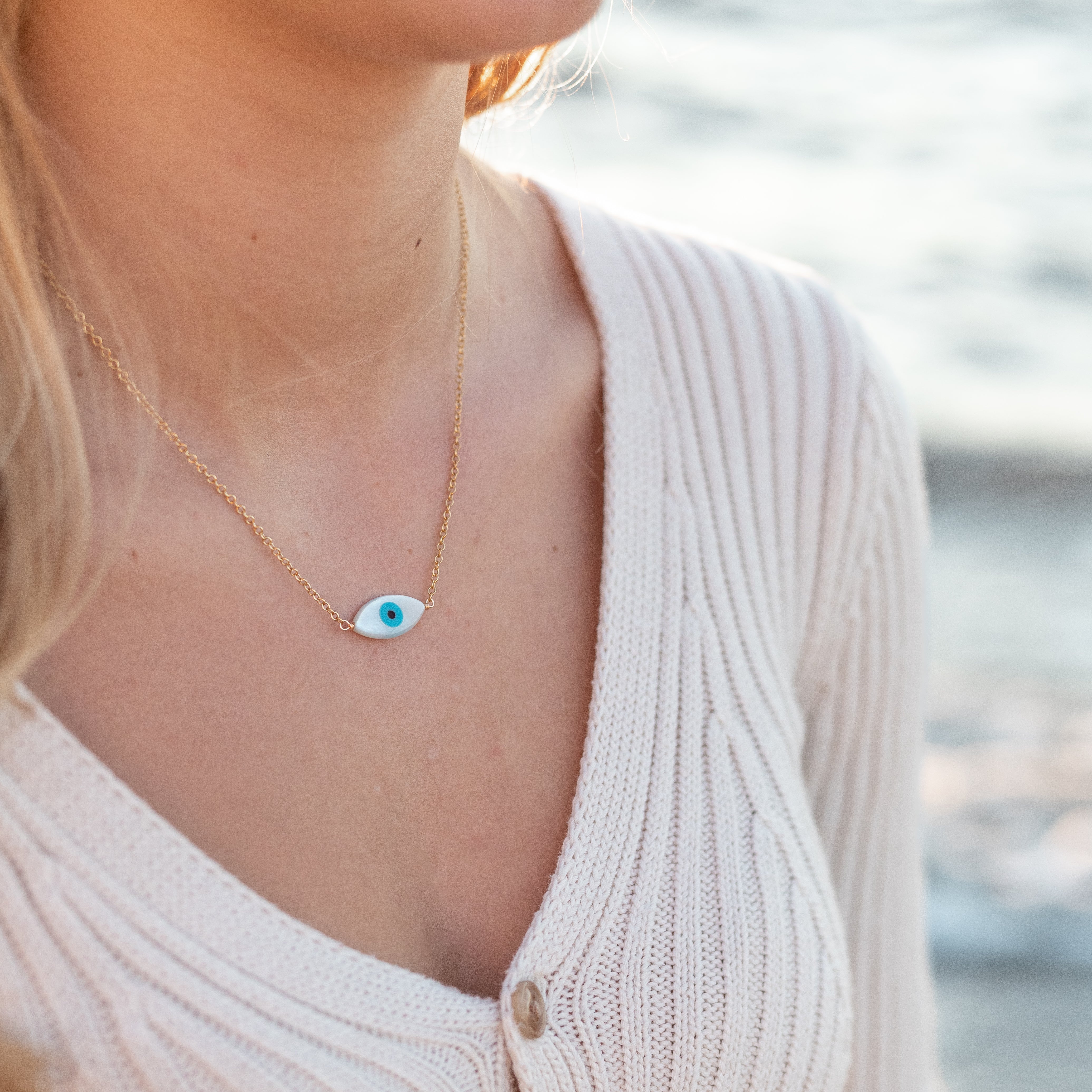 Mother of pearl evil eye charm wire wrapped with gold wire to delicate gold chain. Shown on a woman’s neck. 