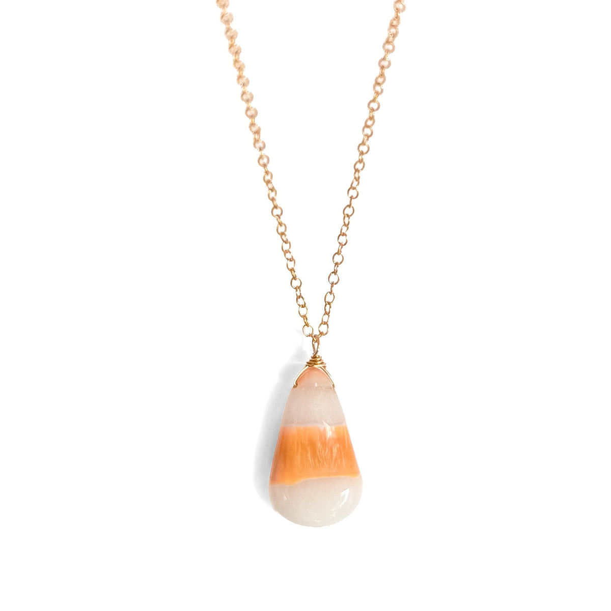 A gold chain necklace with a teardrop-shaped pendant featuring horizontal stripes of orange, cream, and white, styled against a white background with a fuzzy orange pumpkin prop at the top.