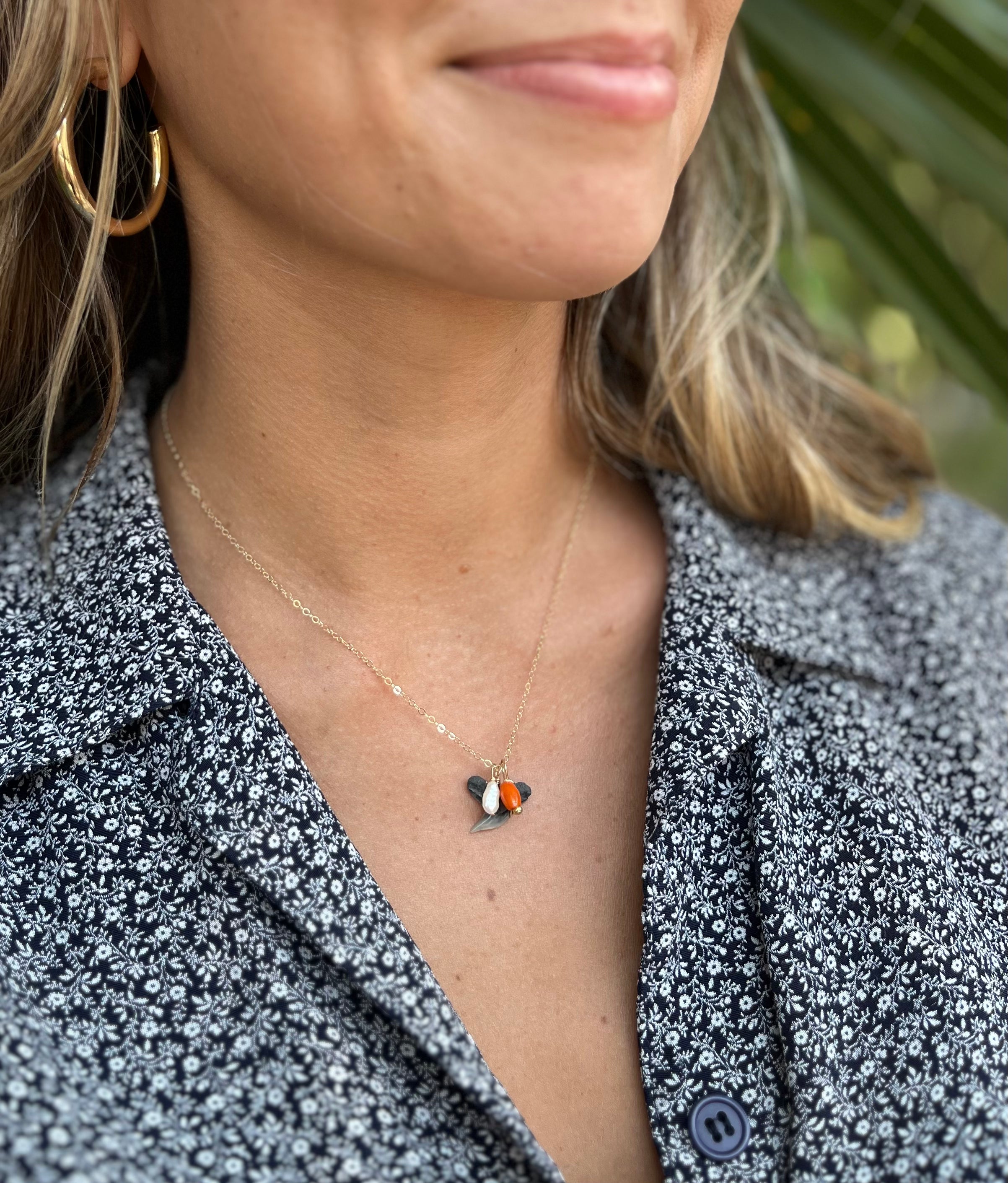 Tiny shark tooth necklace with a pearl and coral on it. Attached to a gold chain. Shown on a woman's neck. 