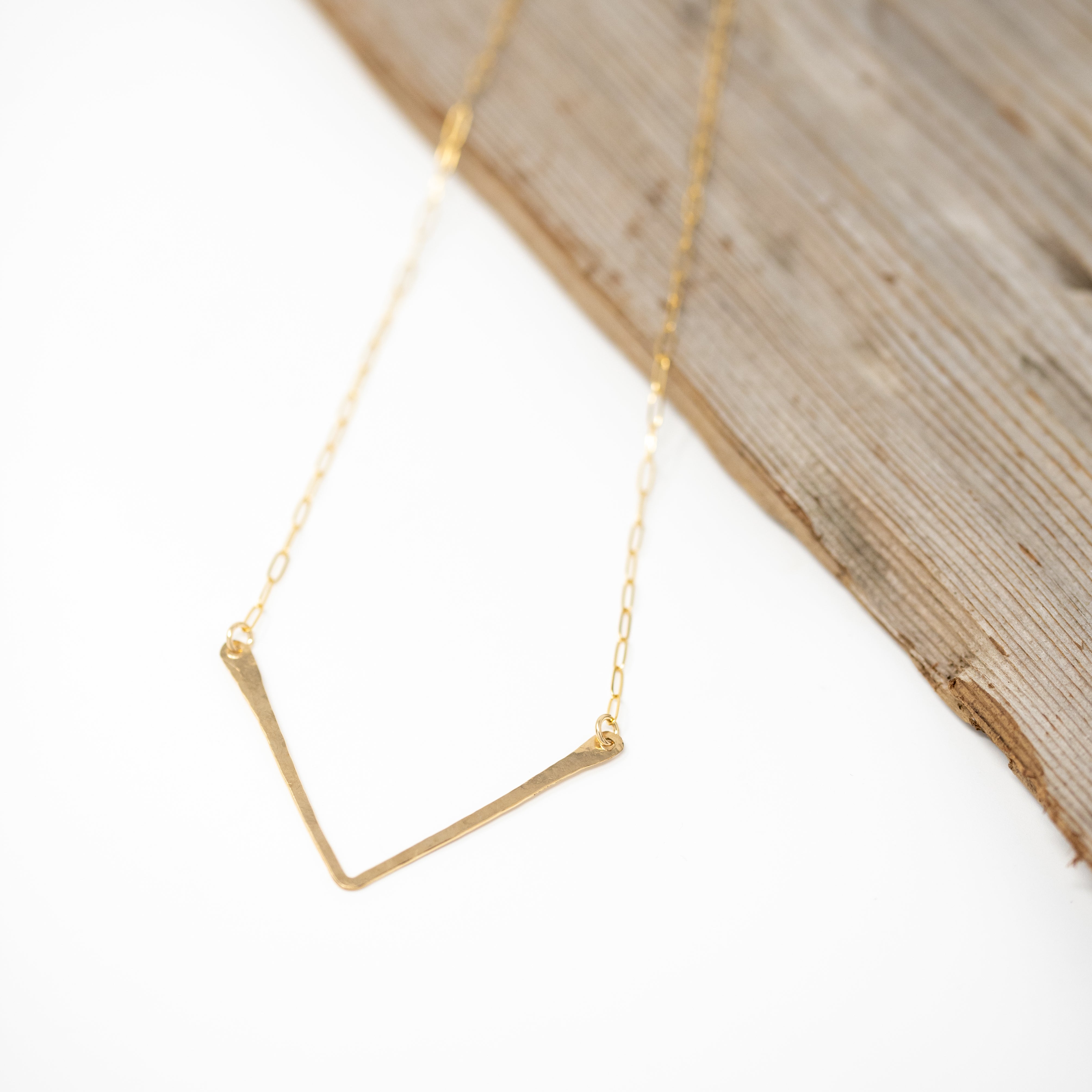 Hand forged V shaped gold bar attached to a gold chain.