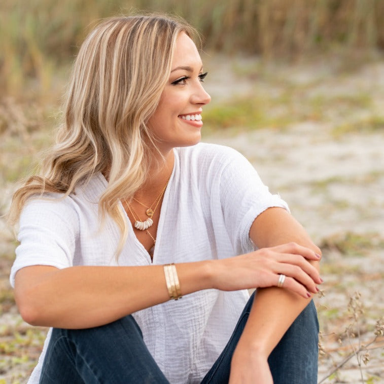 blonde lady sitting on beach wearing 3 gold hammered cuff bracelets