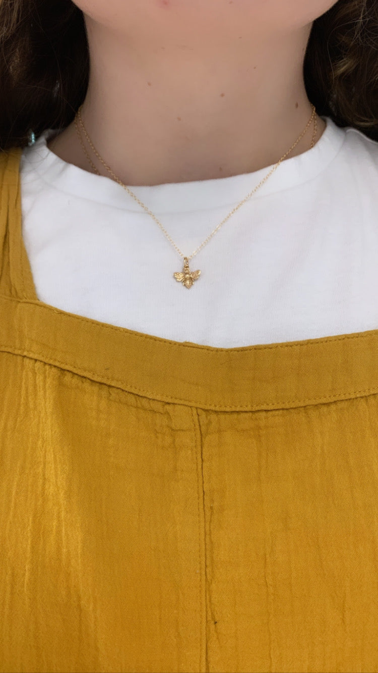 The gold bee charm on a gold chain shown a woman's neck. 