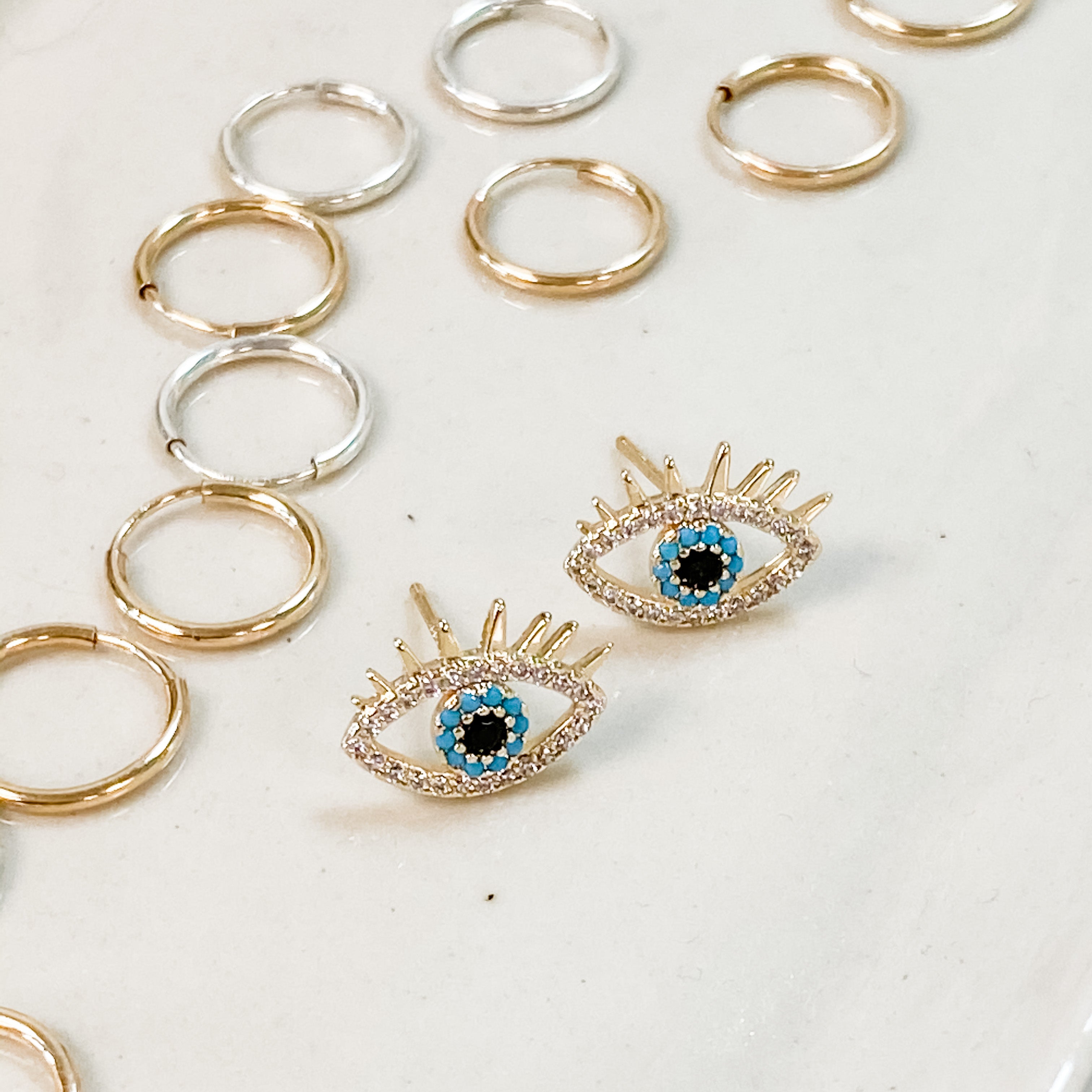 Evil eye stud earrings. Sparkly cubic zirconia and turquoise surrounding the eye. Shown with our second whole small hoops around it. 