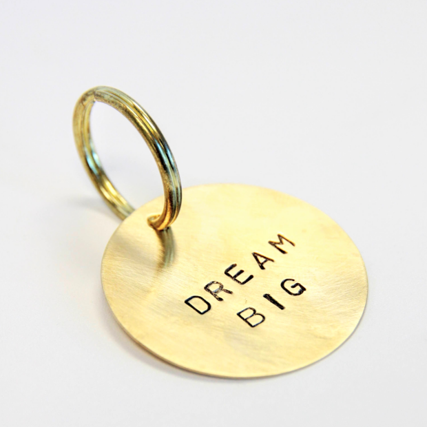 1.5 inch brass keychain with a phrase stamped onto it and a key ring on it.
