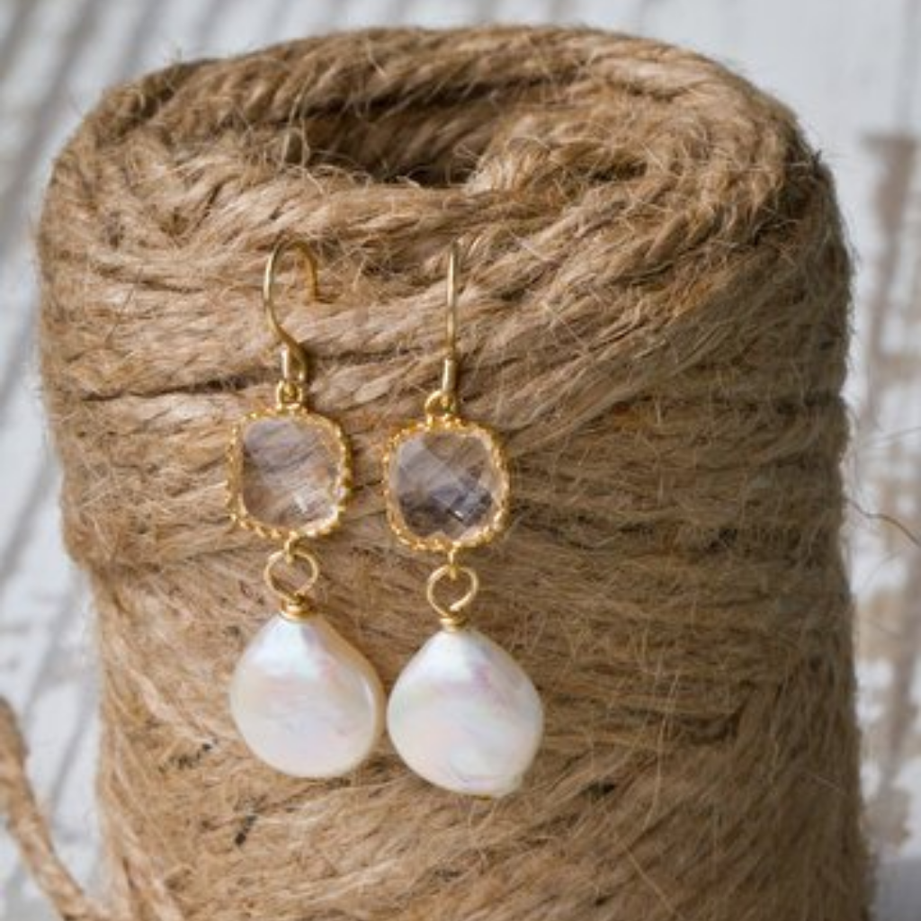 A pair of earrings with crystals wrapped in gold. There is a dime sized pearl hanging from the bottom.