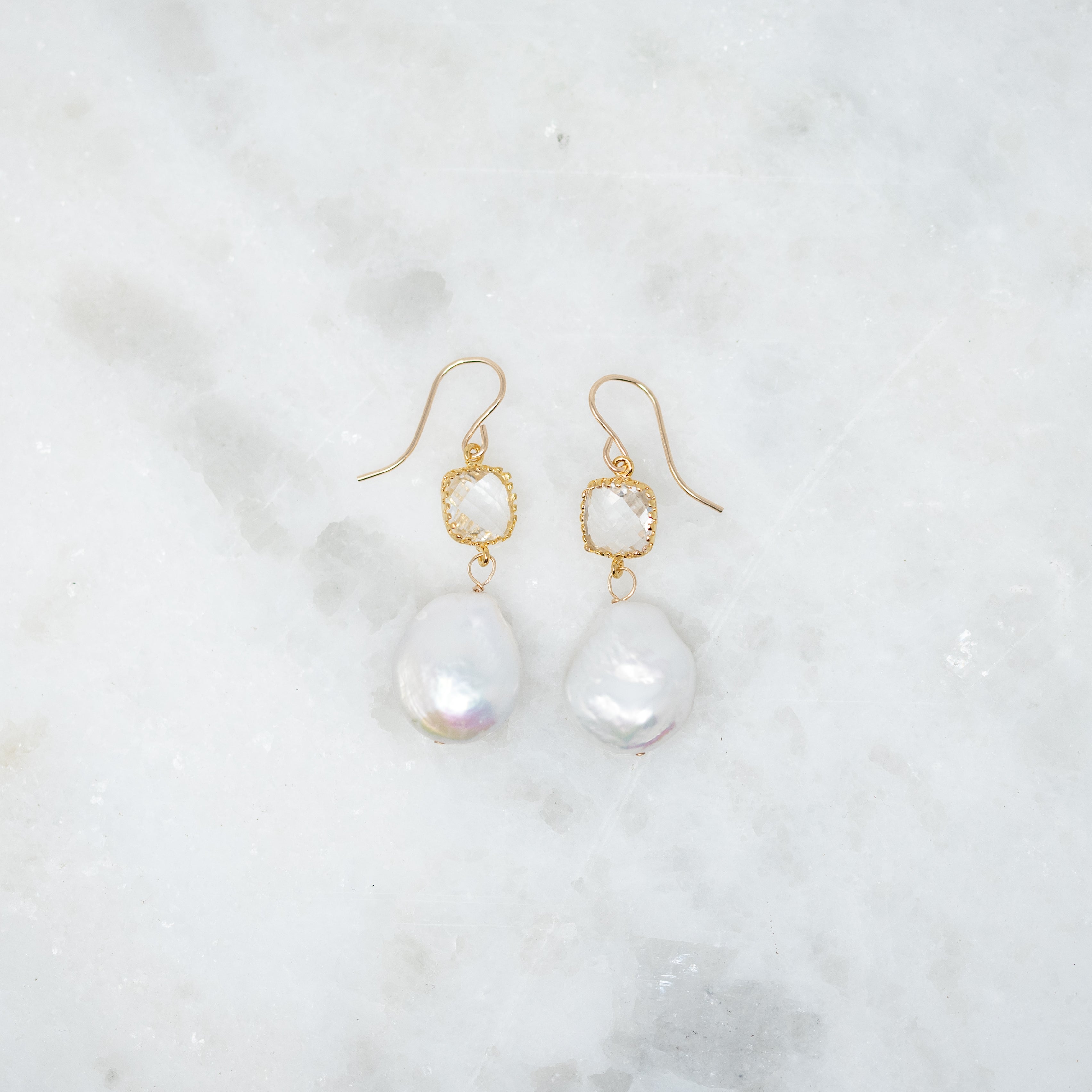 A pair of earrings with crystals wrapped in gold. There is a dime sized pearl hanging from the bottom. 