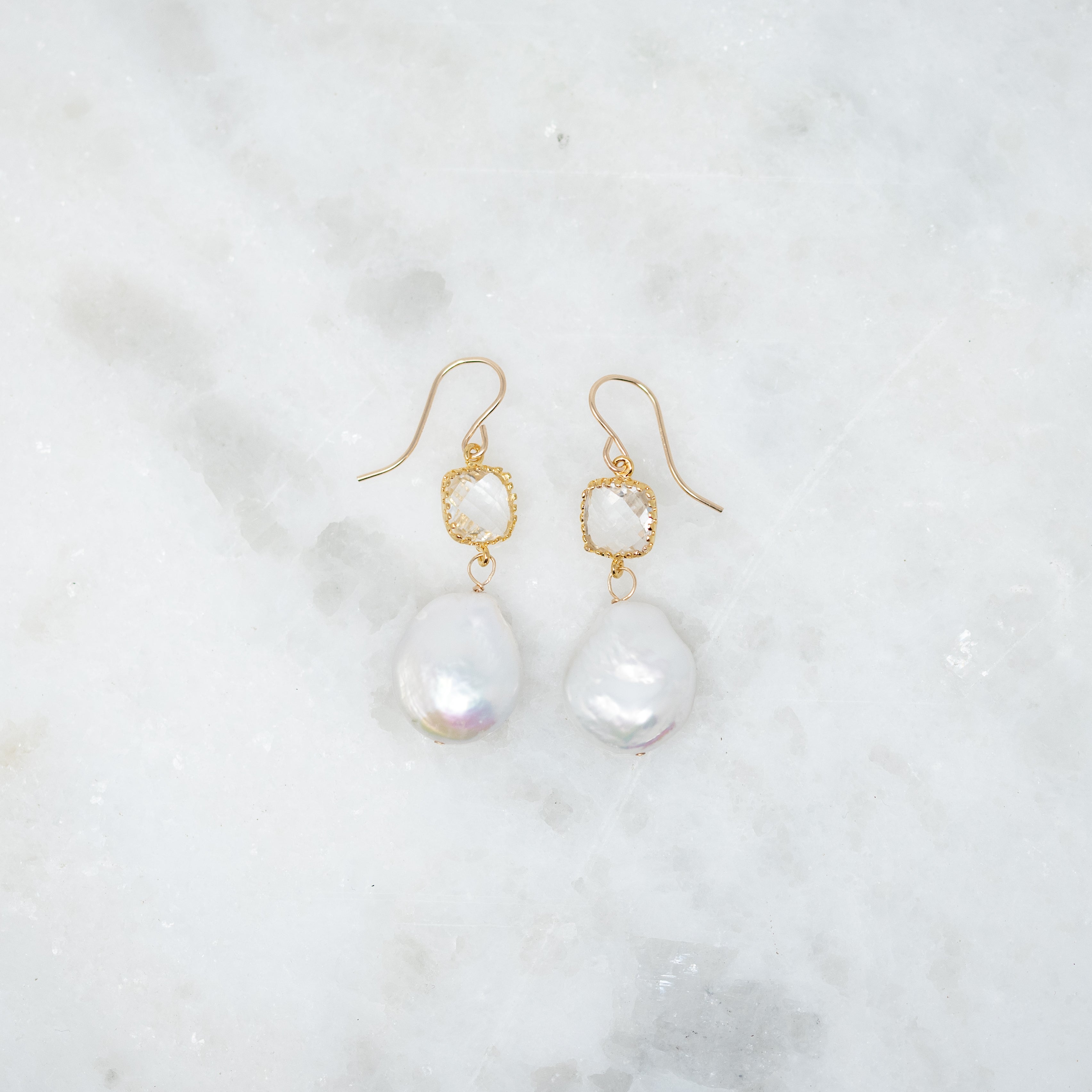 A pair of earrings with crystals wrapped in gold. There is a dime sized pearl hanging from the bottom.