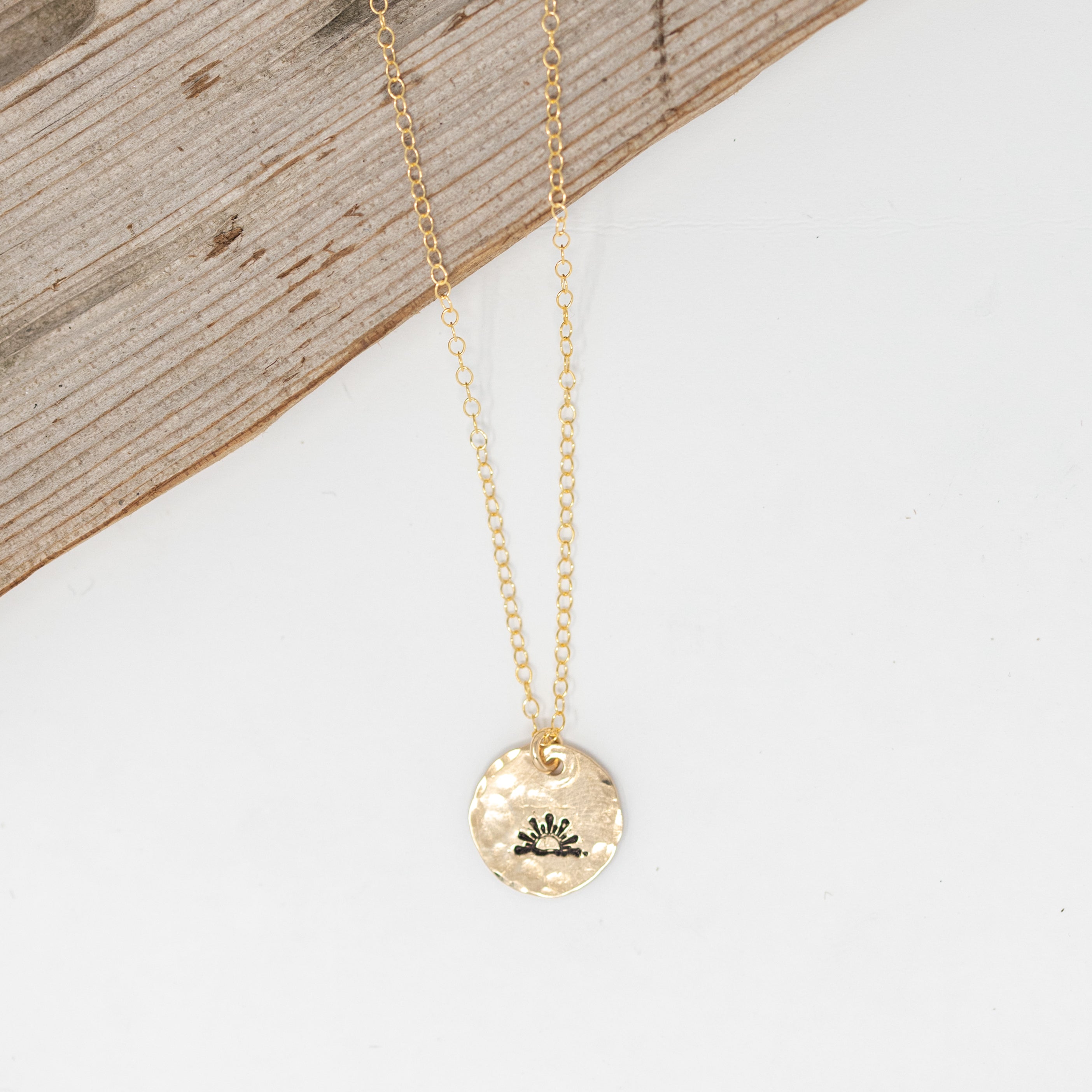 gold filled medium size circle (less than a dime), with a sunset stamped on it, attached to a gold chain